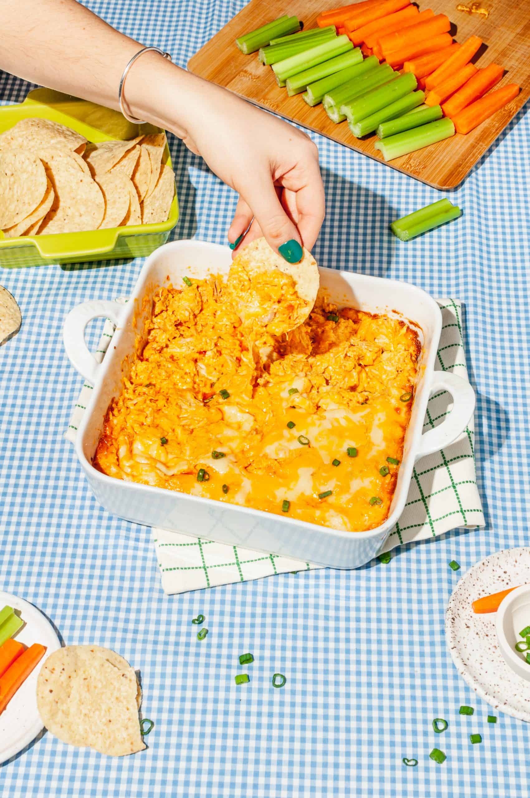 hand dipping tortilla chip into dish of cheesy buffalo chicken dip