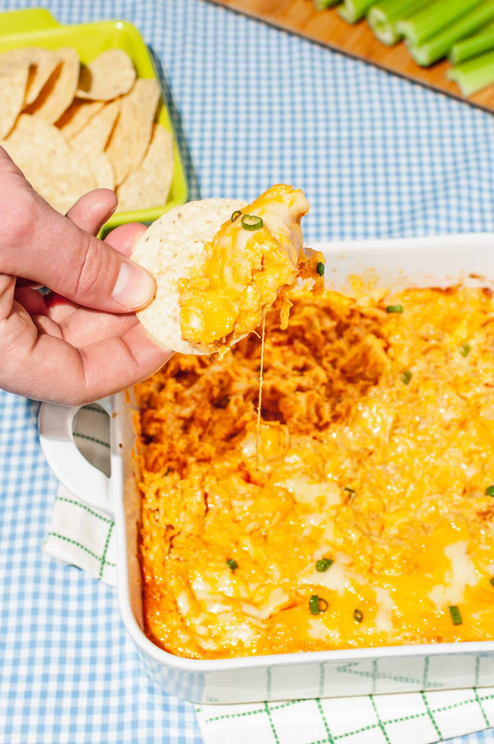 hand dipping tortilla chip into dish of cheesy buffalo chicken dip