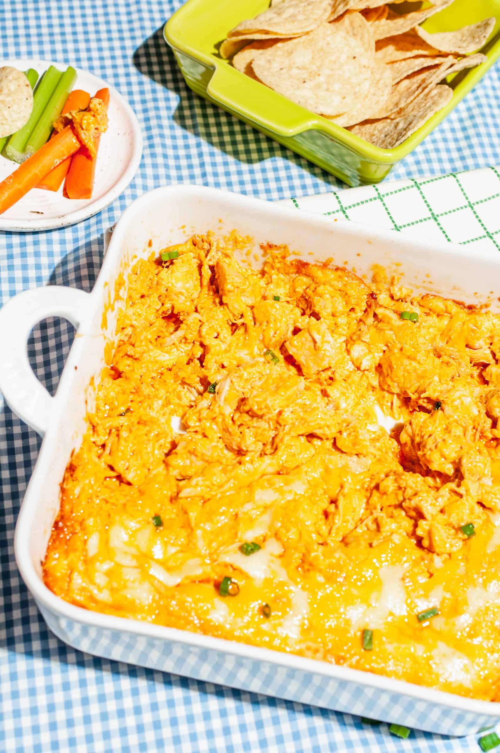 cheesy buffalo chicken dip in white baking dish with bowl of tortilla chips on the side