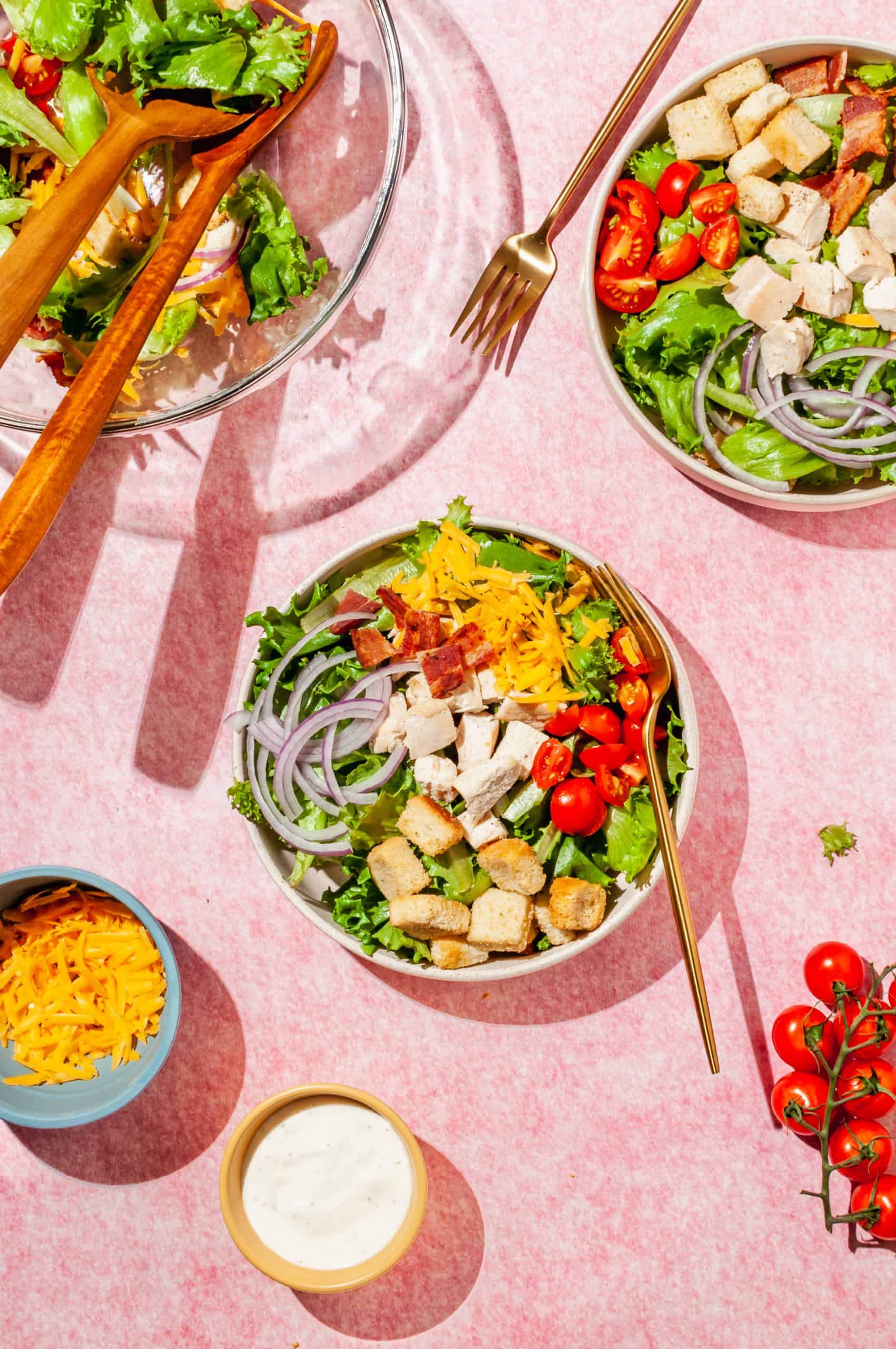 two bowls with chicken bacon salad before adding ranch dressing, extra salad in large bowl to the side