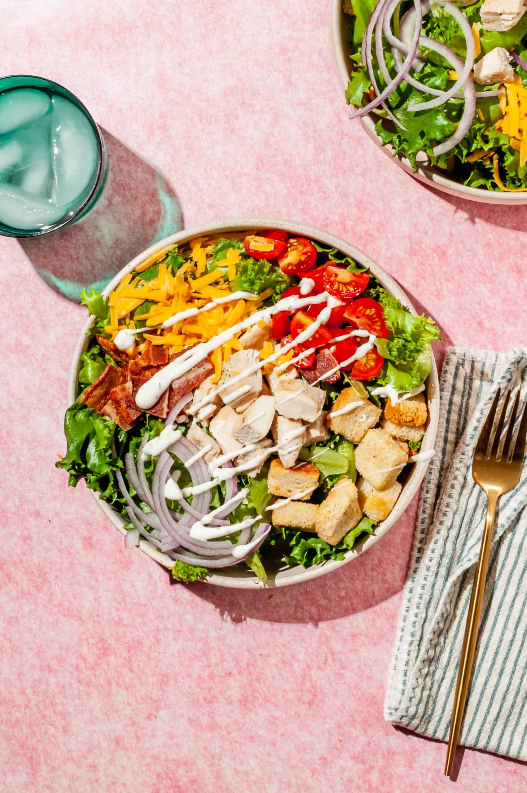 chicken bacon ranch salad in a shallow bowl with a teal glass of ice water on the side