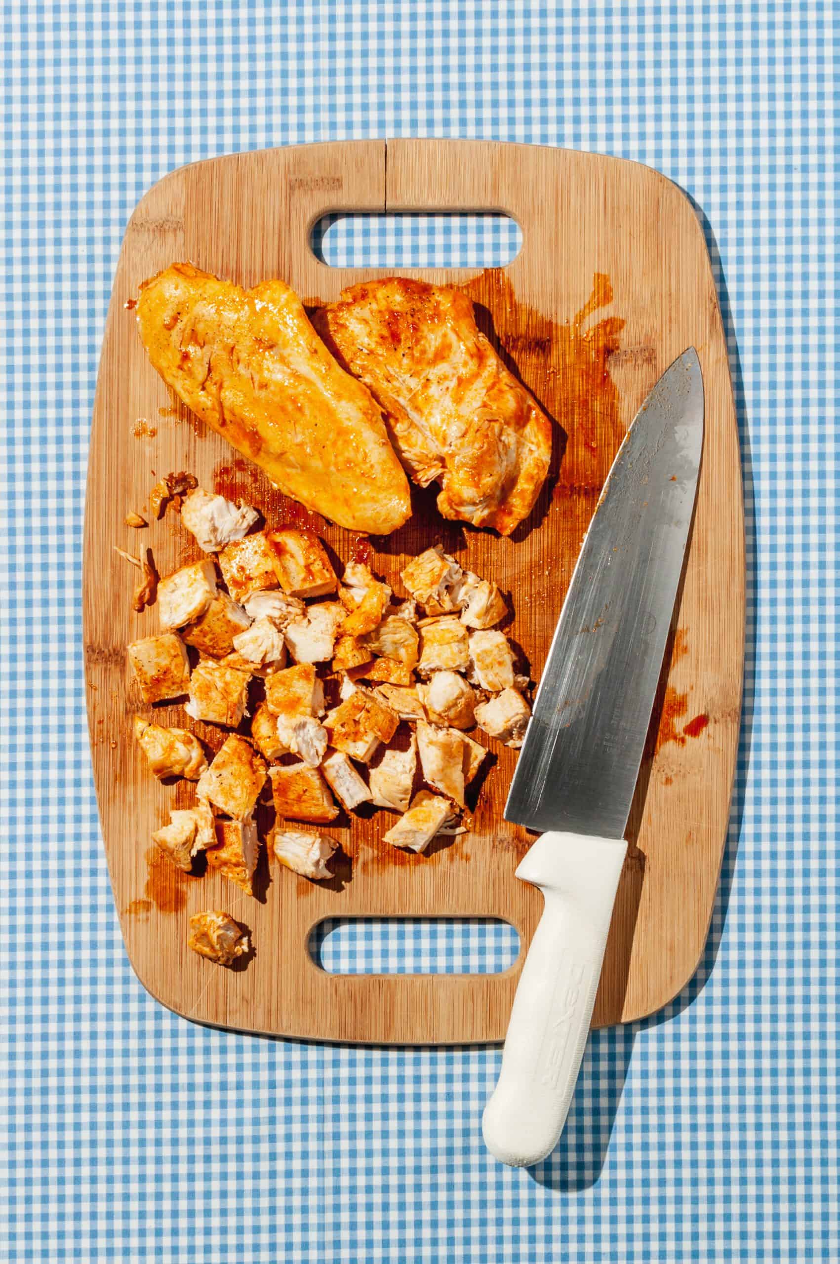 chicken breast lightly coated in hot sauce on a cutting board, some diced some whole