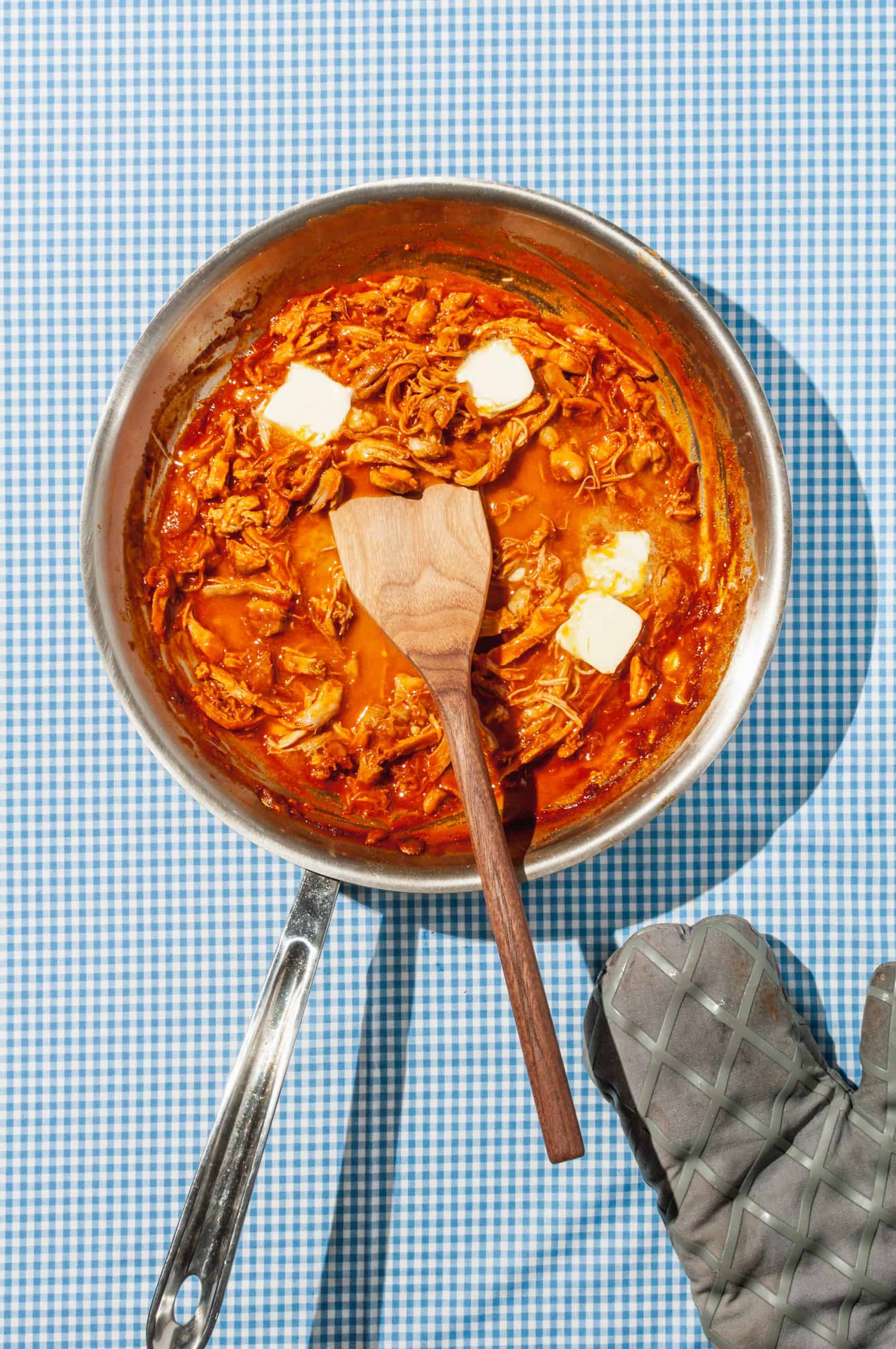 melting butter in pan with shredded chicken in buffalo sauce