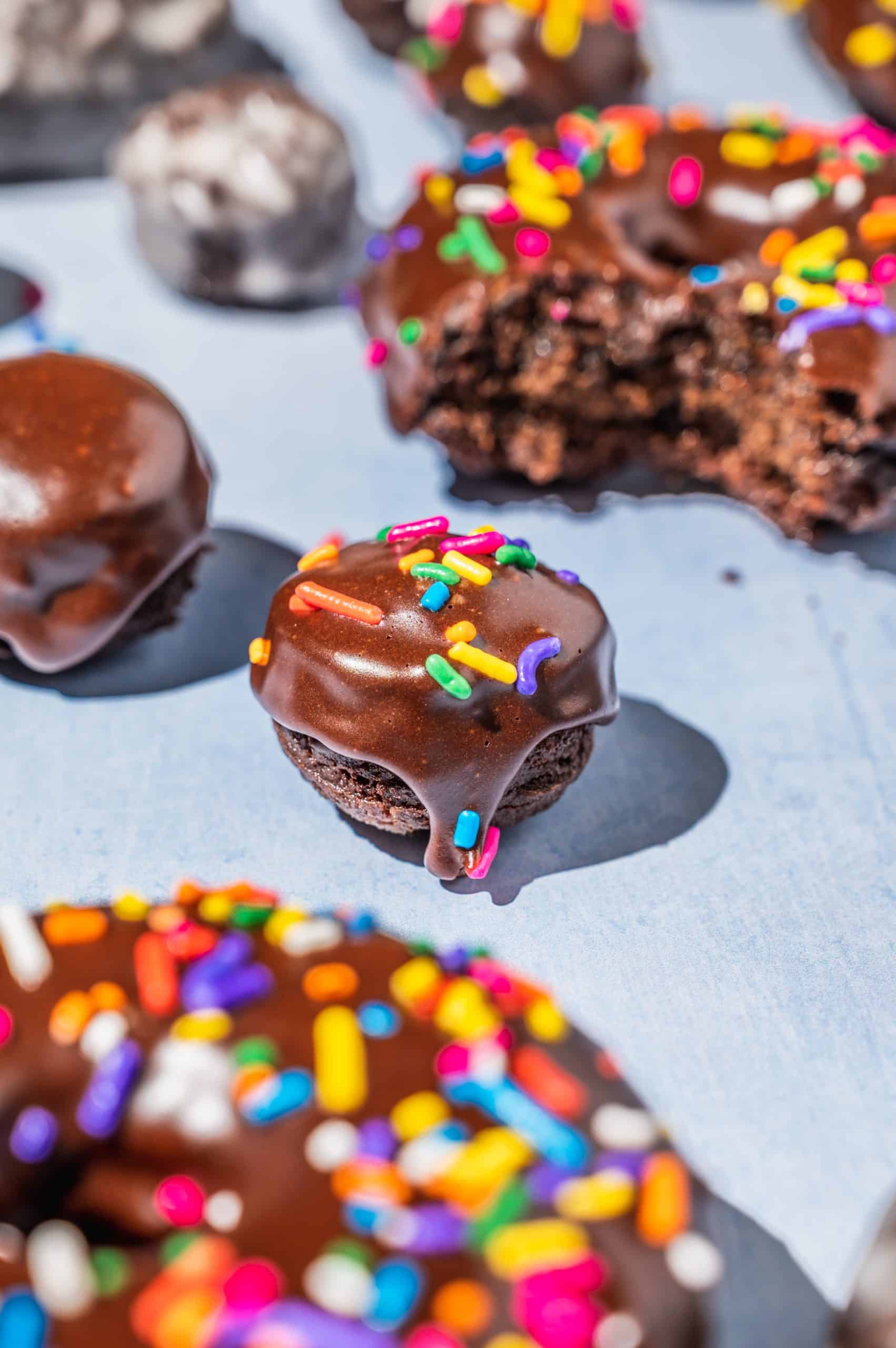 chocolate cake donut hole with chocolate glaze and rainbow sprinkles surrounded by more donuts
