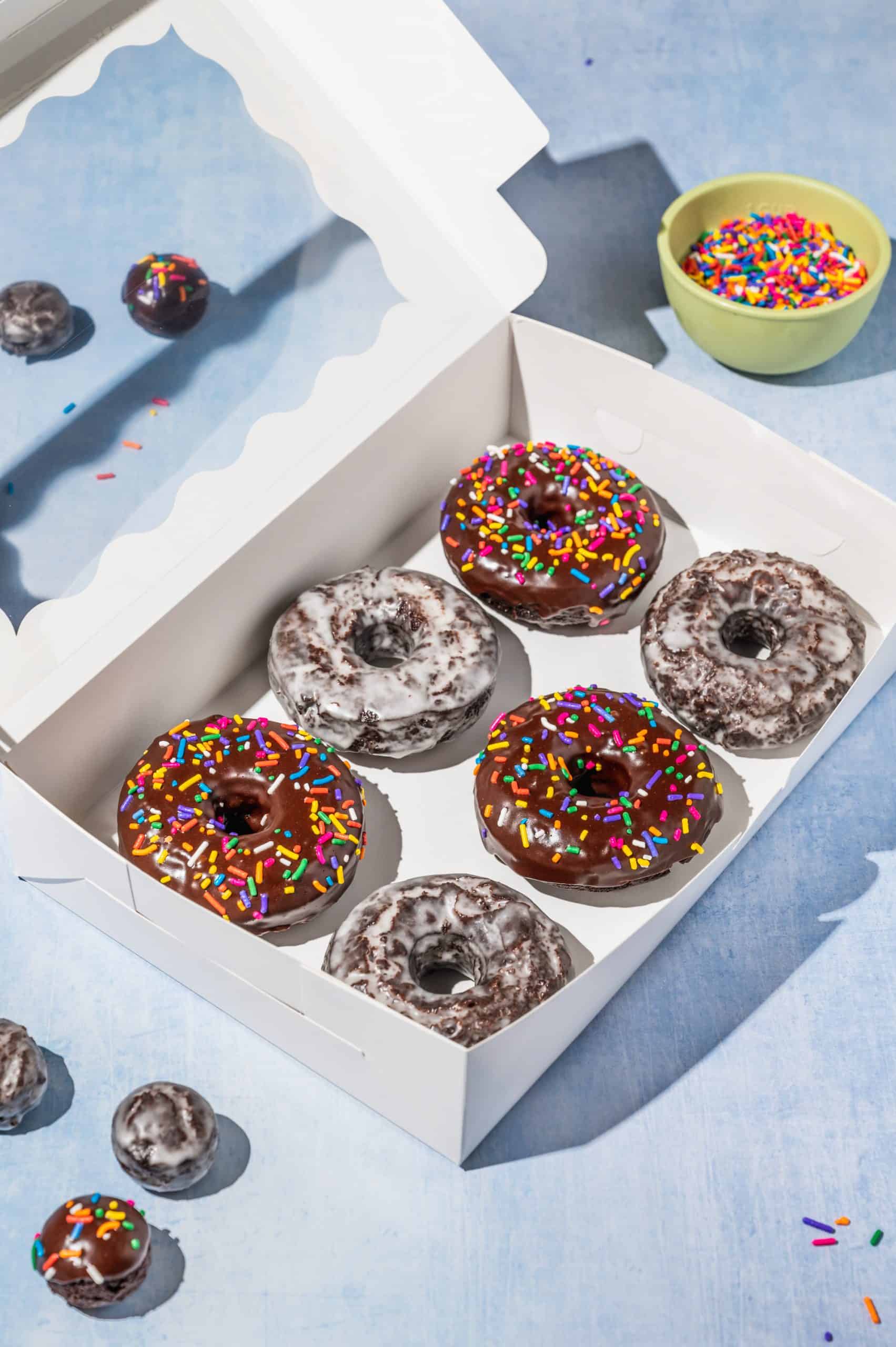 white box with half dozen chocolate donuts (3 glazed, 3 chocolate frosted with sprinkles)