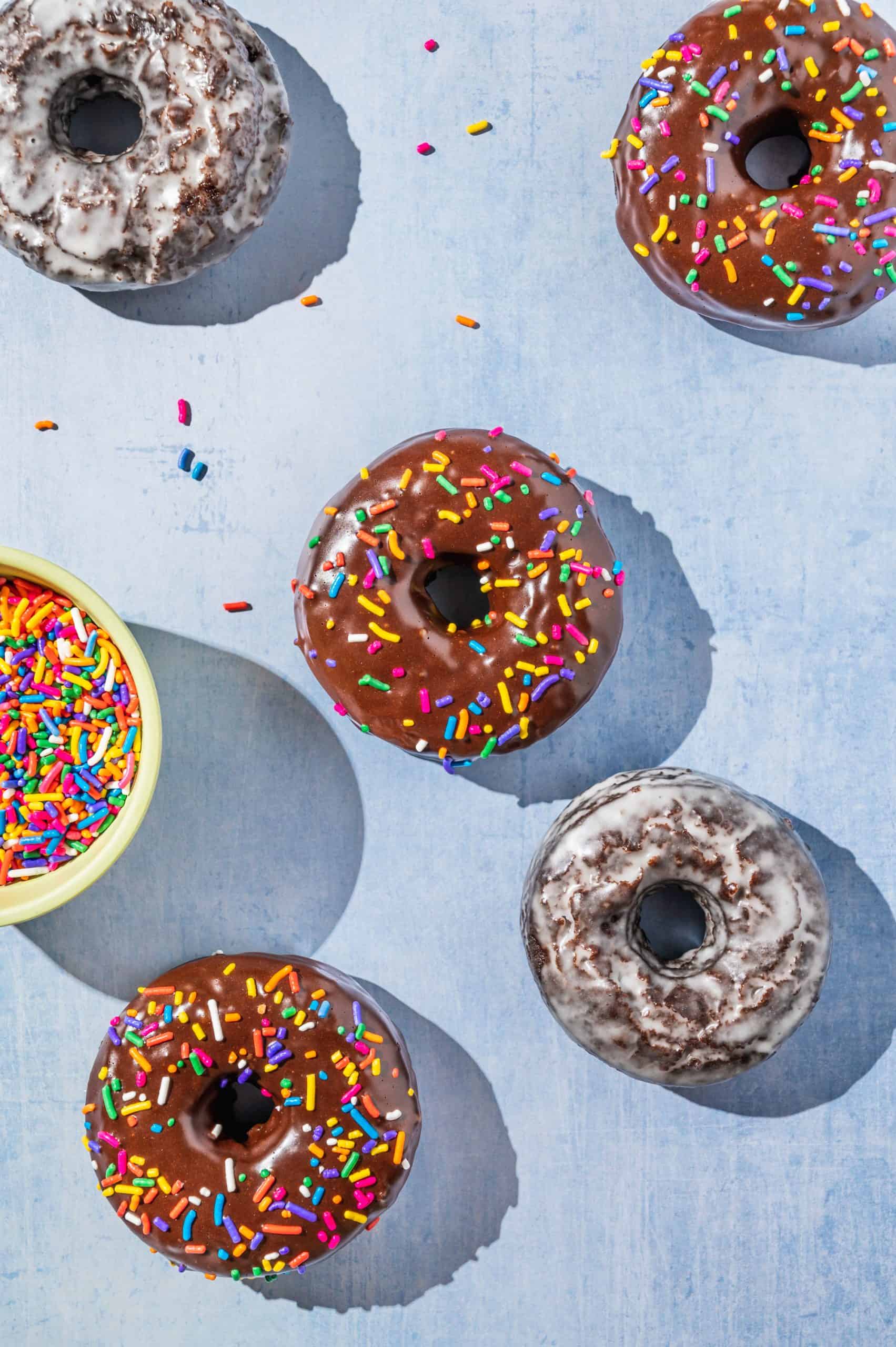 3 chocolate frosted donuts with sprinkles and 2 glazed chocolate cake donuts on a blue background