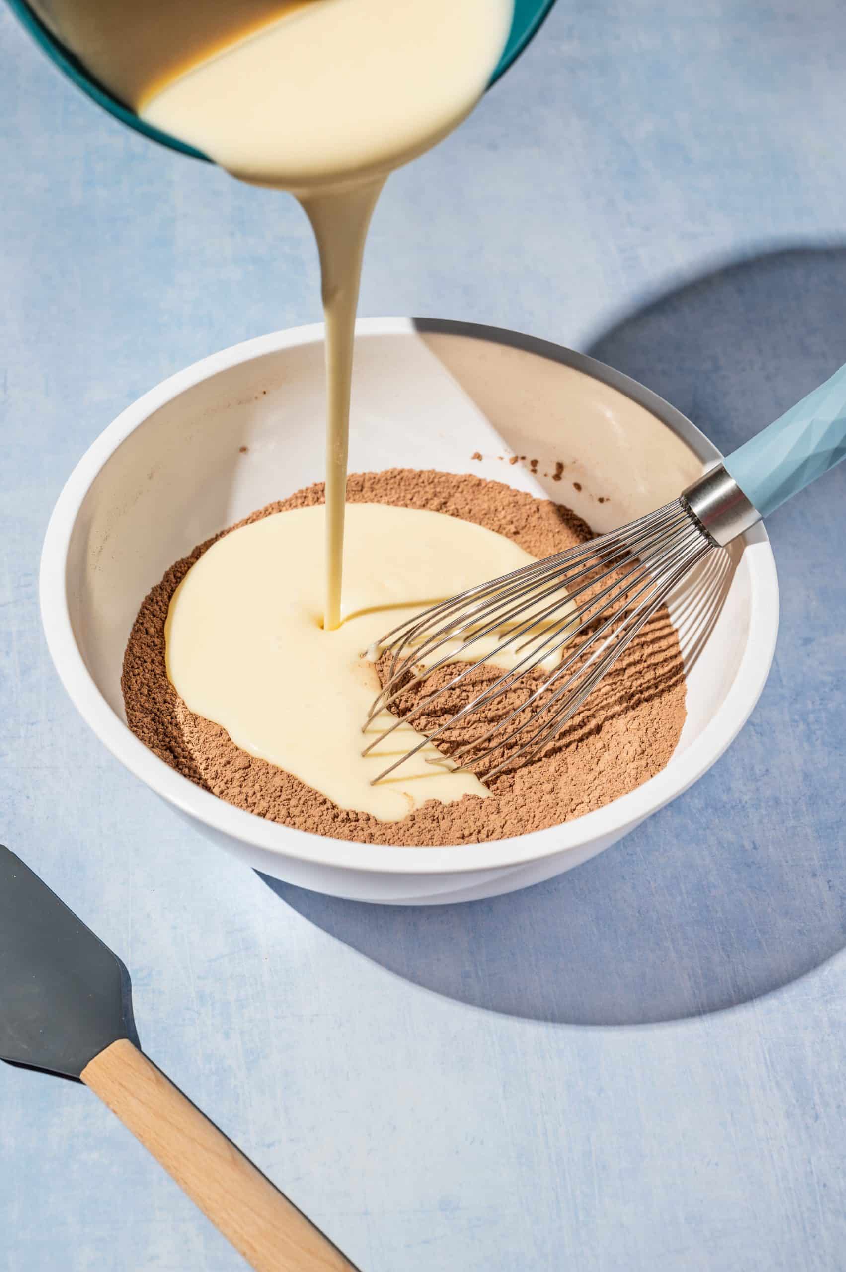 pouring creamy liquid mixture into a bowl with cocoa power and flour mixture