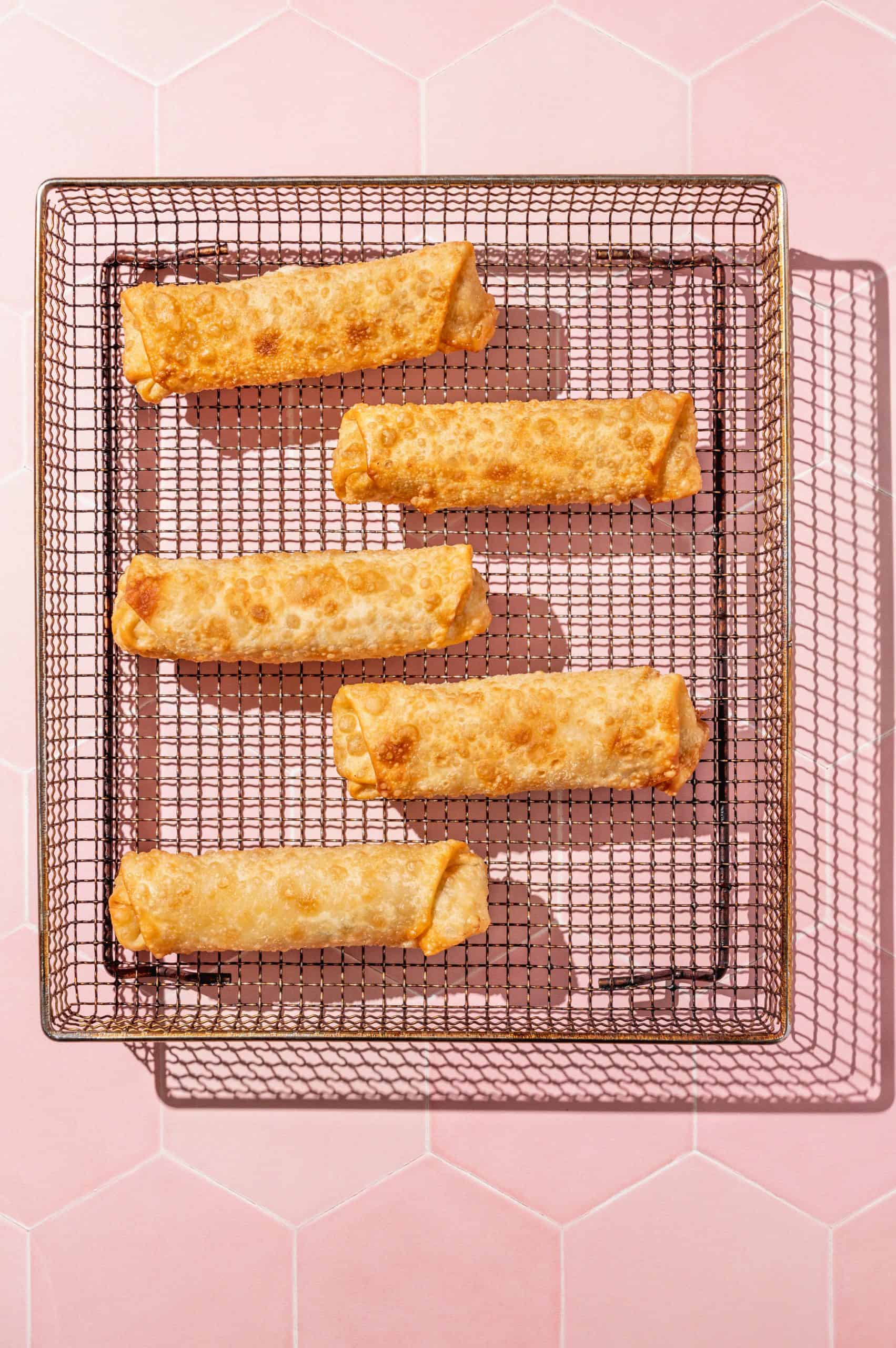 5 crispy crab rangoon egg rolls on an air fryer tray