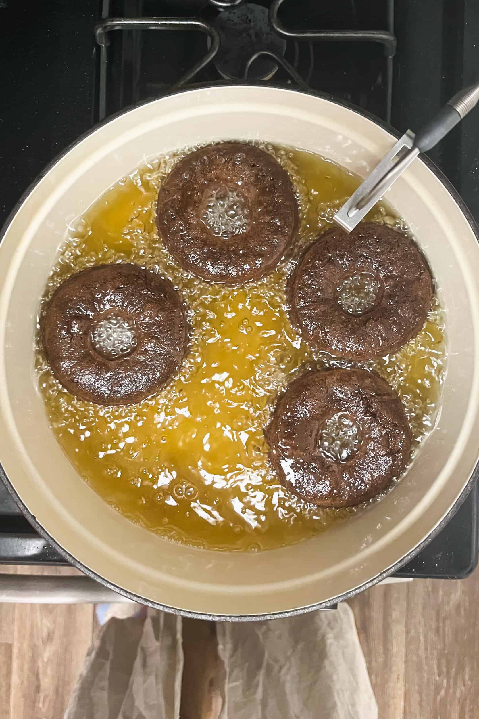 4 chocolate cake donuts floating in a pot of oil on the stove for deep frying
