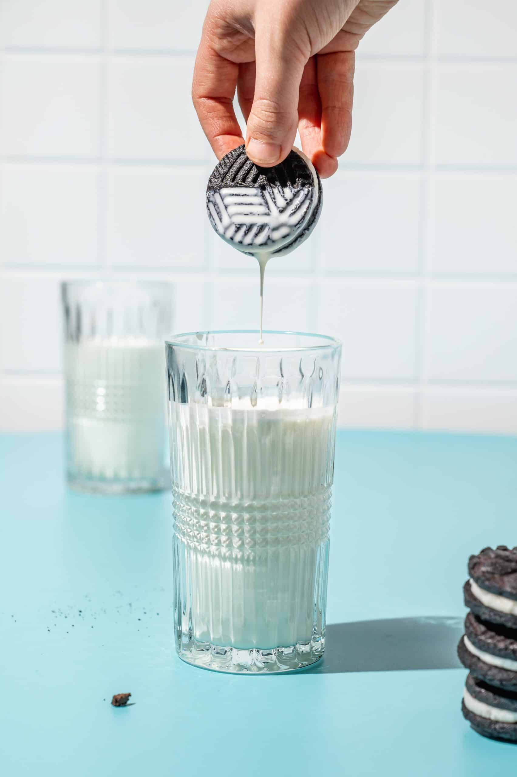 hand dipping a homemade oreo in a glass of milk, milk dripping off of cookie
