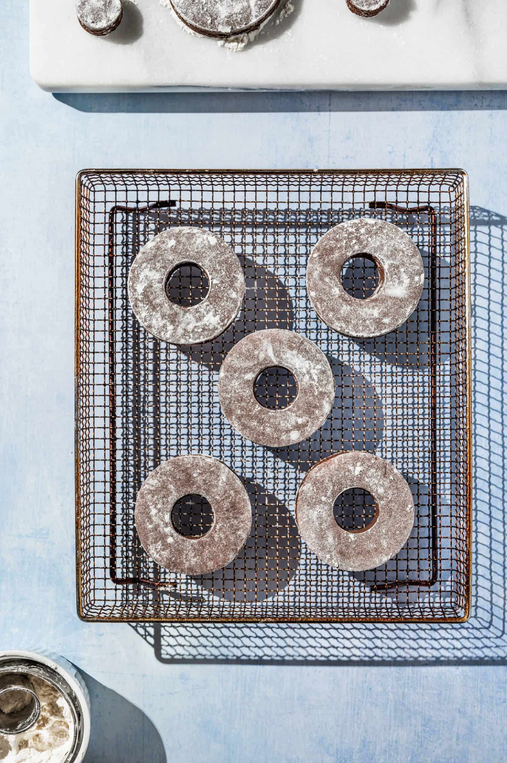 5 chocolate cake donuts dusted with flour on an air fryer tray before cooking