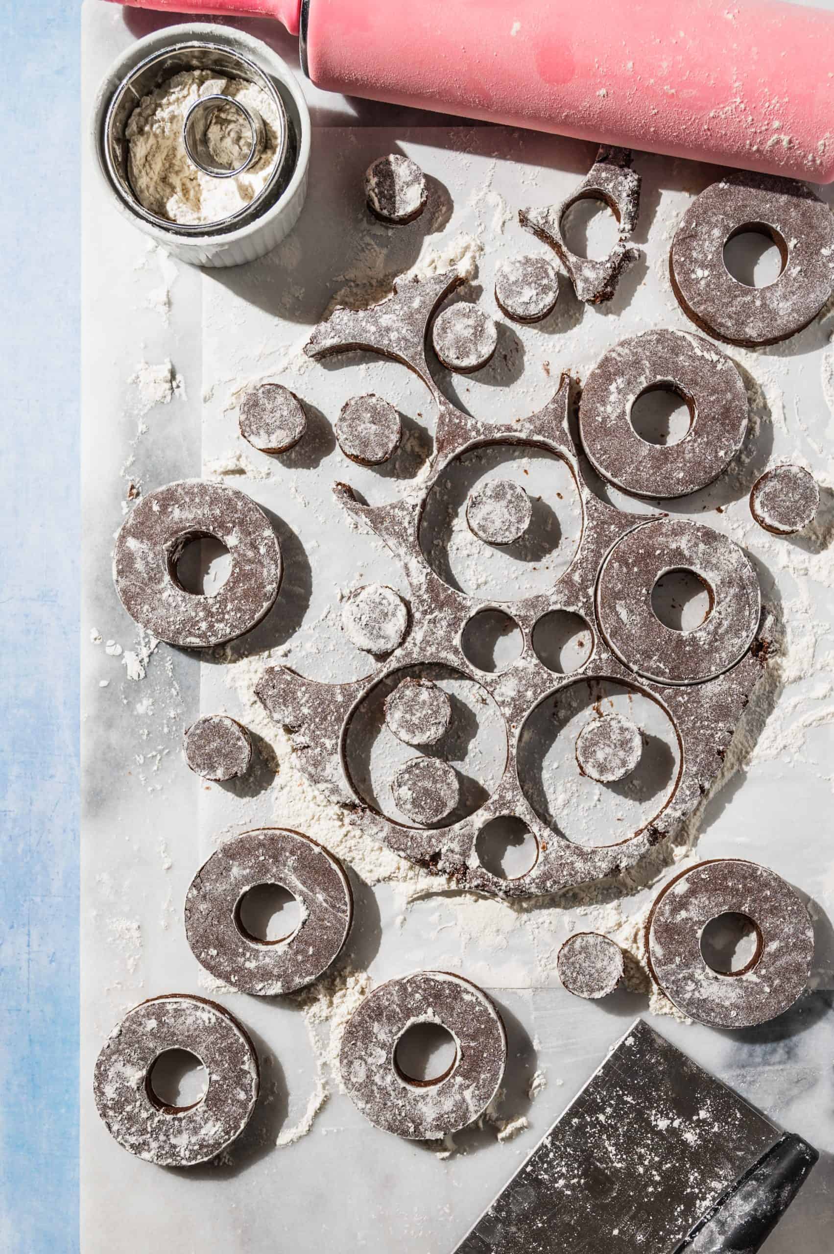 chocolate dough rolled out on marble with 8 donuts and lots of donut holes stamped out