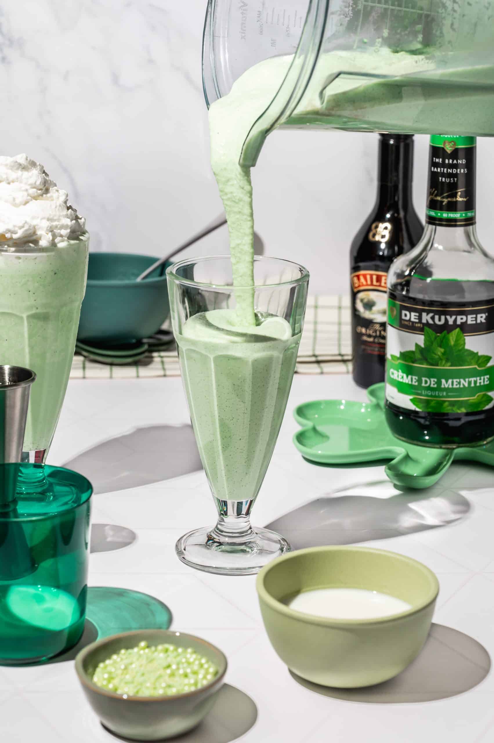 pouring green shamrock shake mixture into a milkshake glass