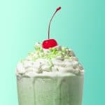 close up of top of an alcoholic shamrock shake in a glass with whipped cream, green sprinkles, and a cherry on top