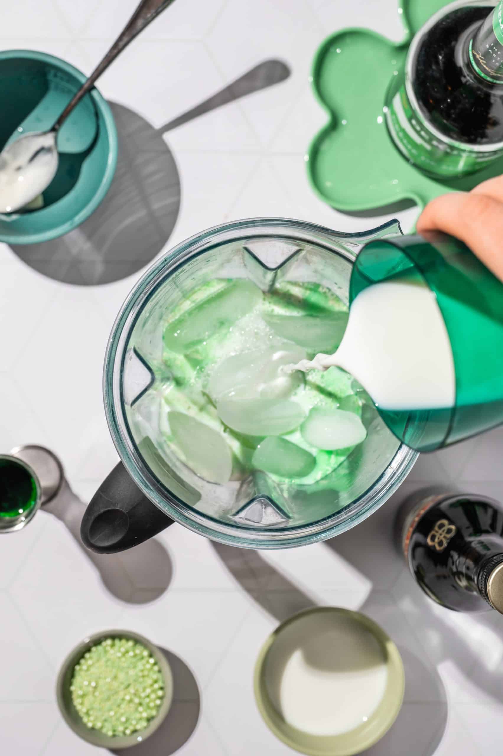 pouring milk into blender bowl filled with ice, ice cream, creme de menthe and Irish cream liqueur