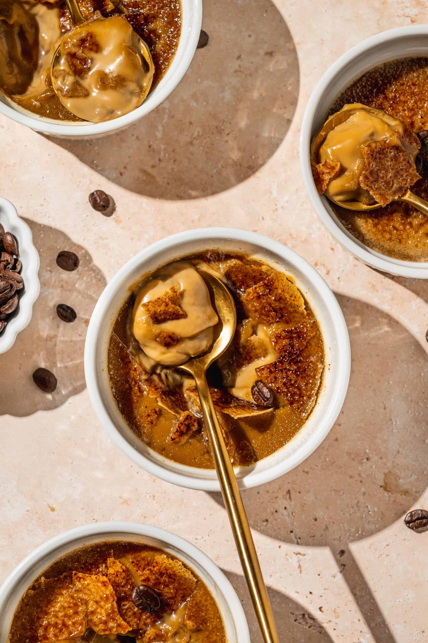 ramekin with coffee creme brulee broken into to show creamy inside and shards of caramelized sugar on the spoon