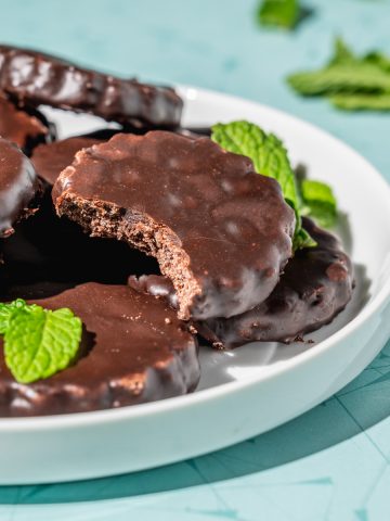 copycat thin mints on a white platter, one with a bite out to show crisp interior