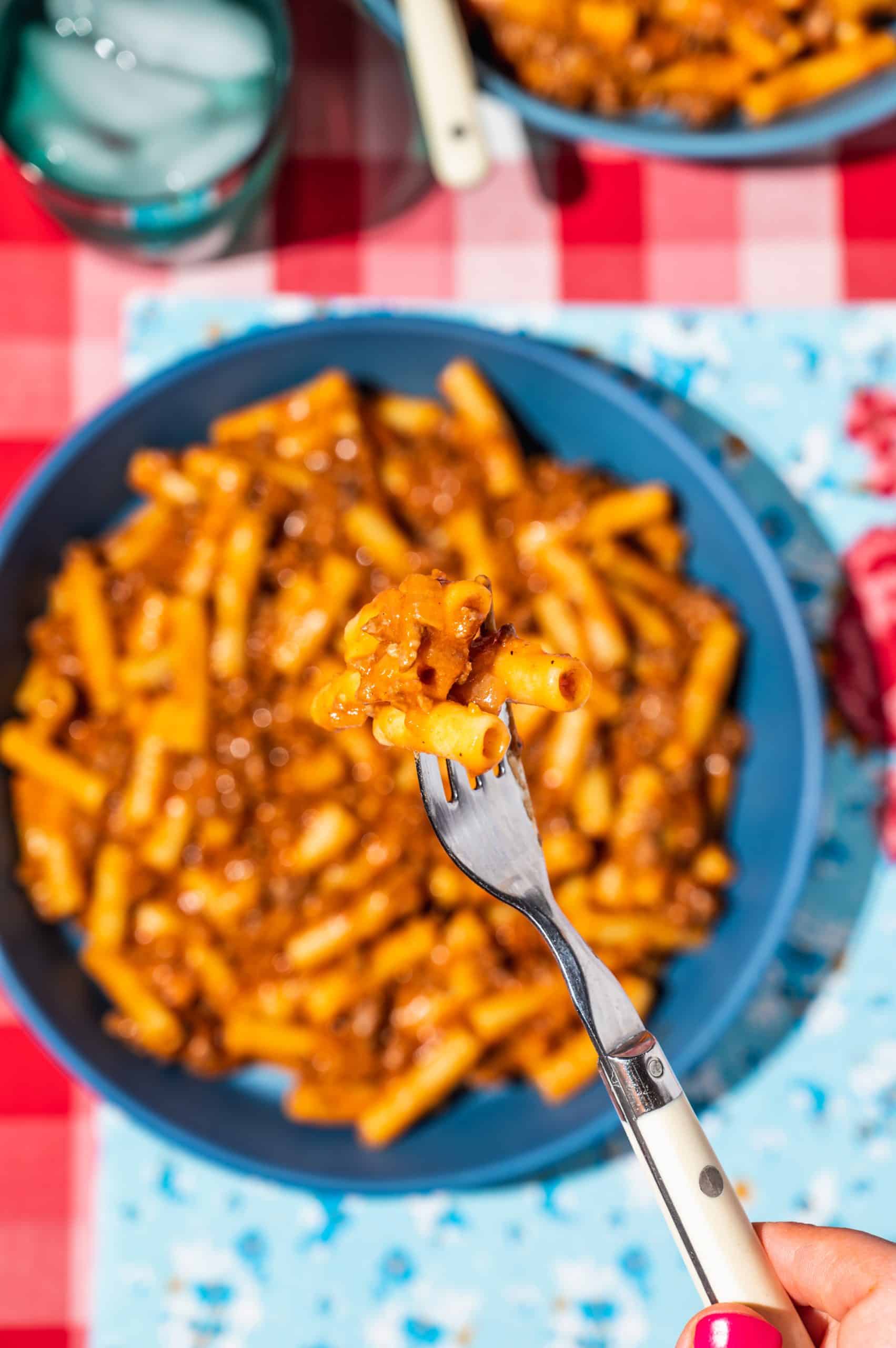 forkful of homemade beefroni held over a blue bowl on a floral placemat