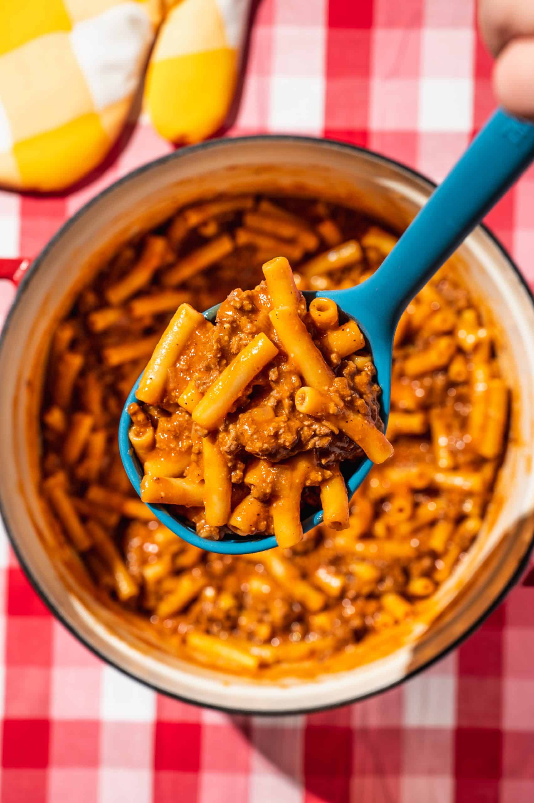 blue ladle filled with homemade beefaroni held over a pot