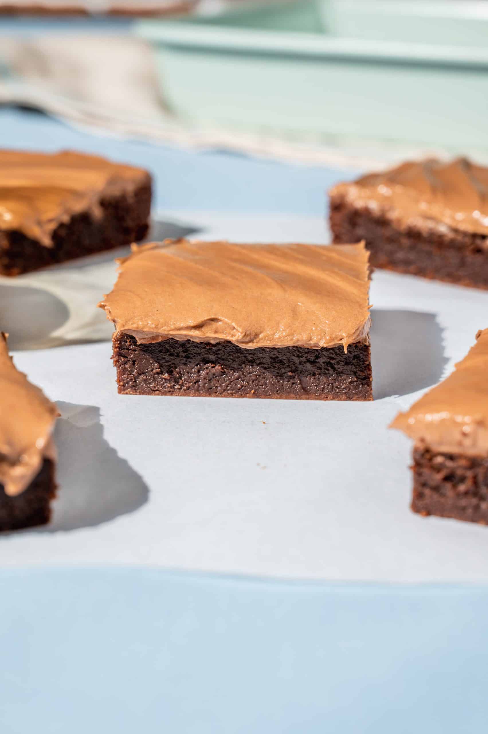 nutella brownie with nutella frosting on white parchment paper on a blue tablecloth