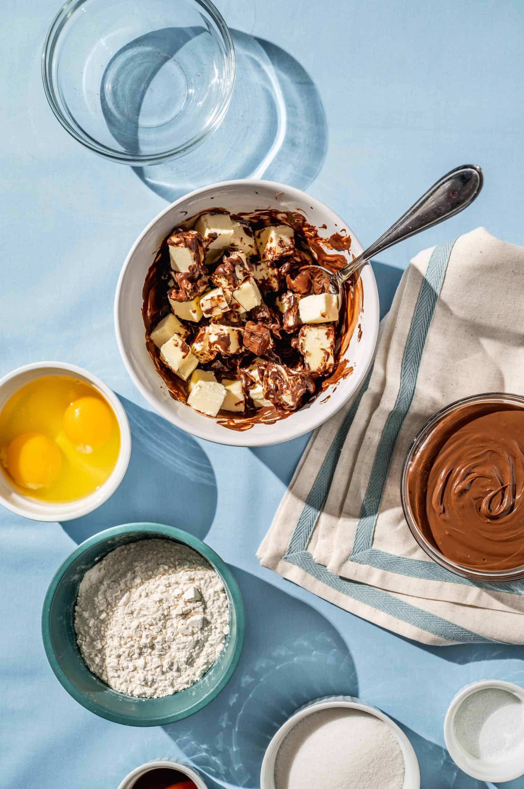 bowl with cubed butter and chocolate partially melted, bowl of nutella and other ingredients to the side