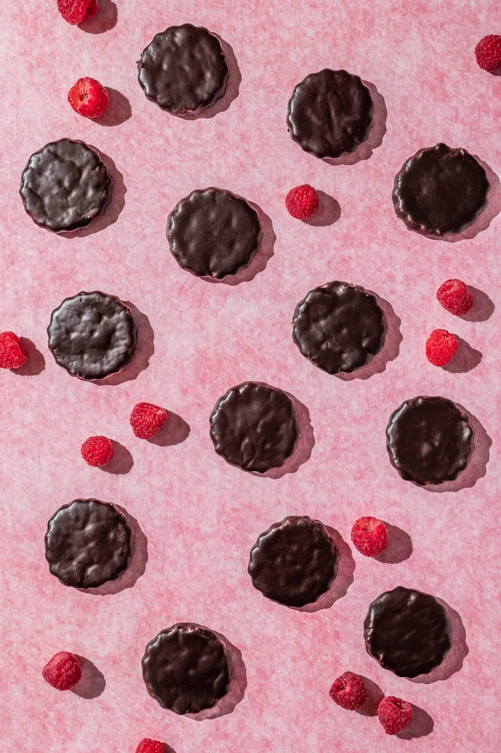 raspberry rally cookies and fresh raspberries spread out on a pink textured background