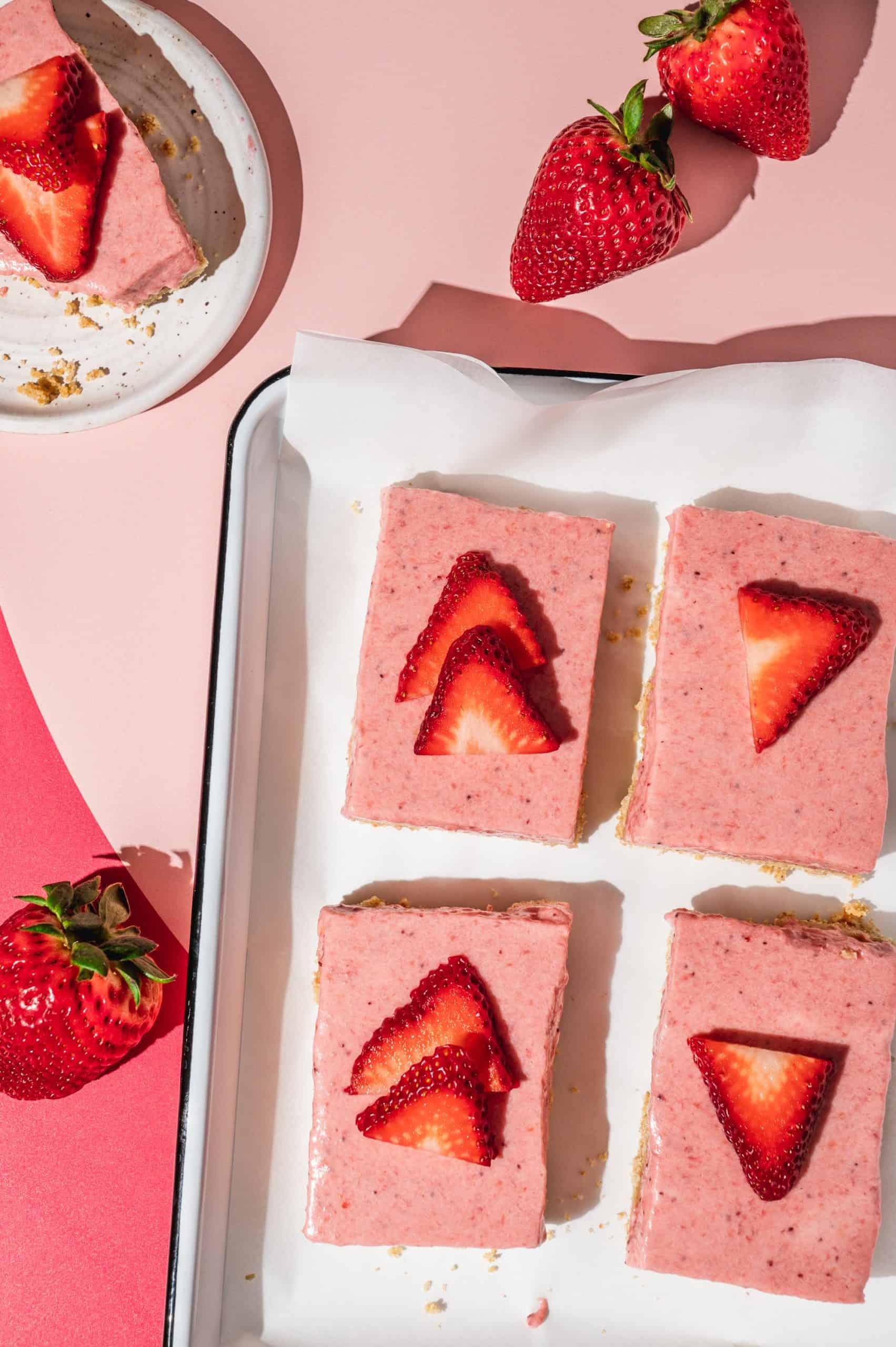 four strawberry pie bars garnished with sliced strawberries on a white tray overhead