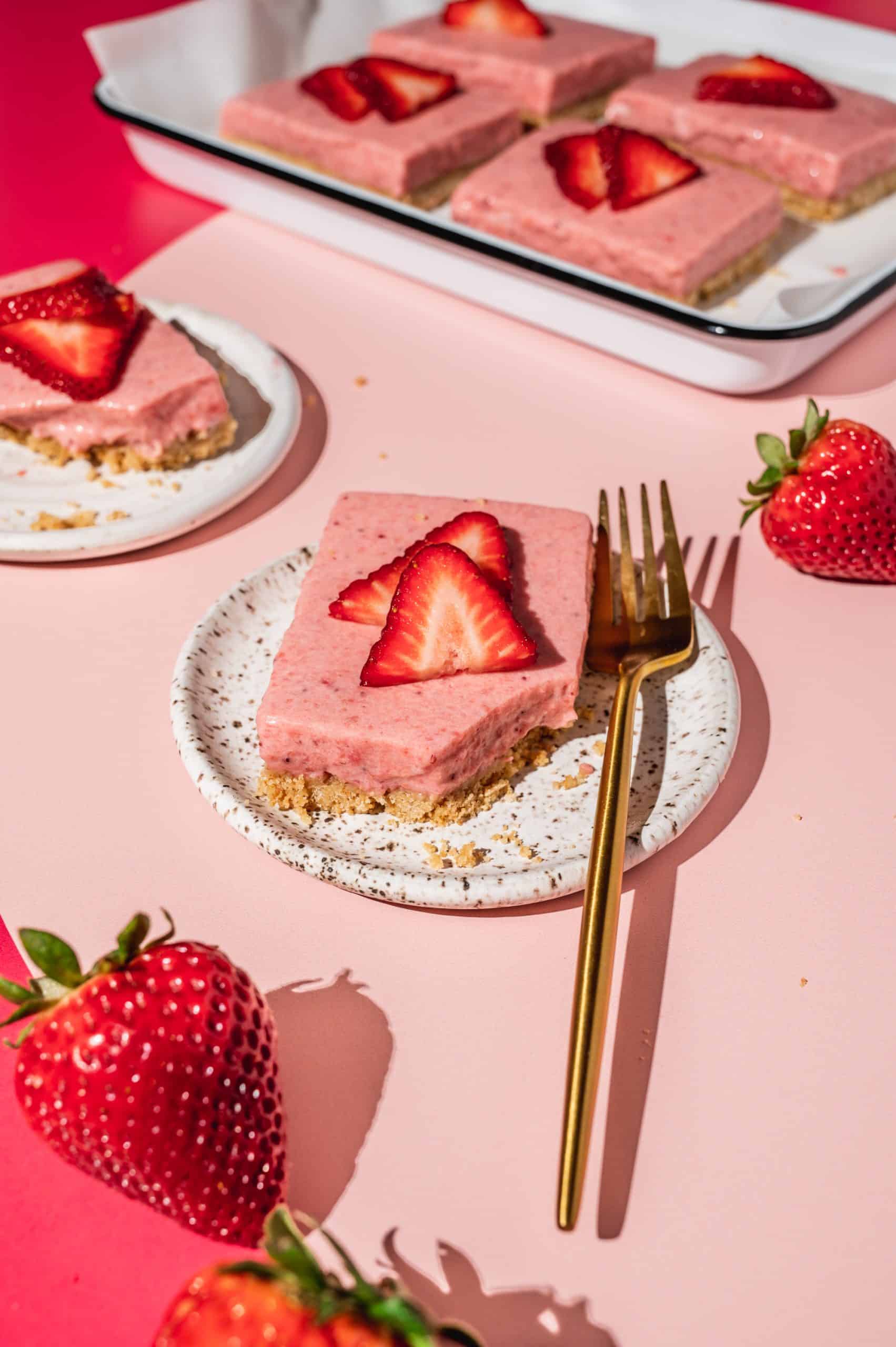strawberry pie bar on a plate with a bite taken out, tray with more strawberry bars in the background