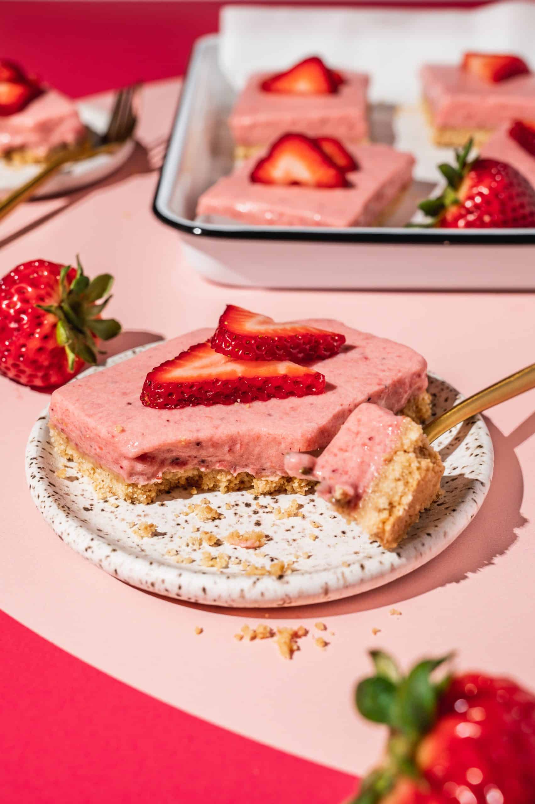 strawberry pie bar on a plate with a bite taken out, tray with strawberry bars in the background