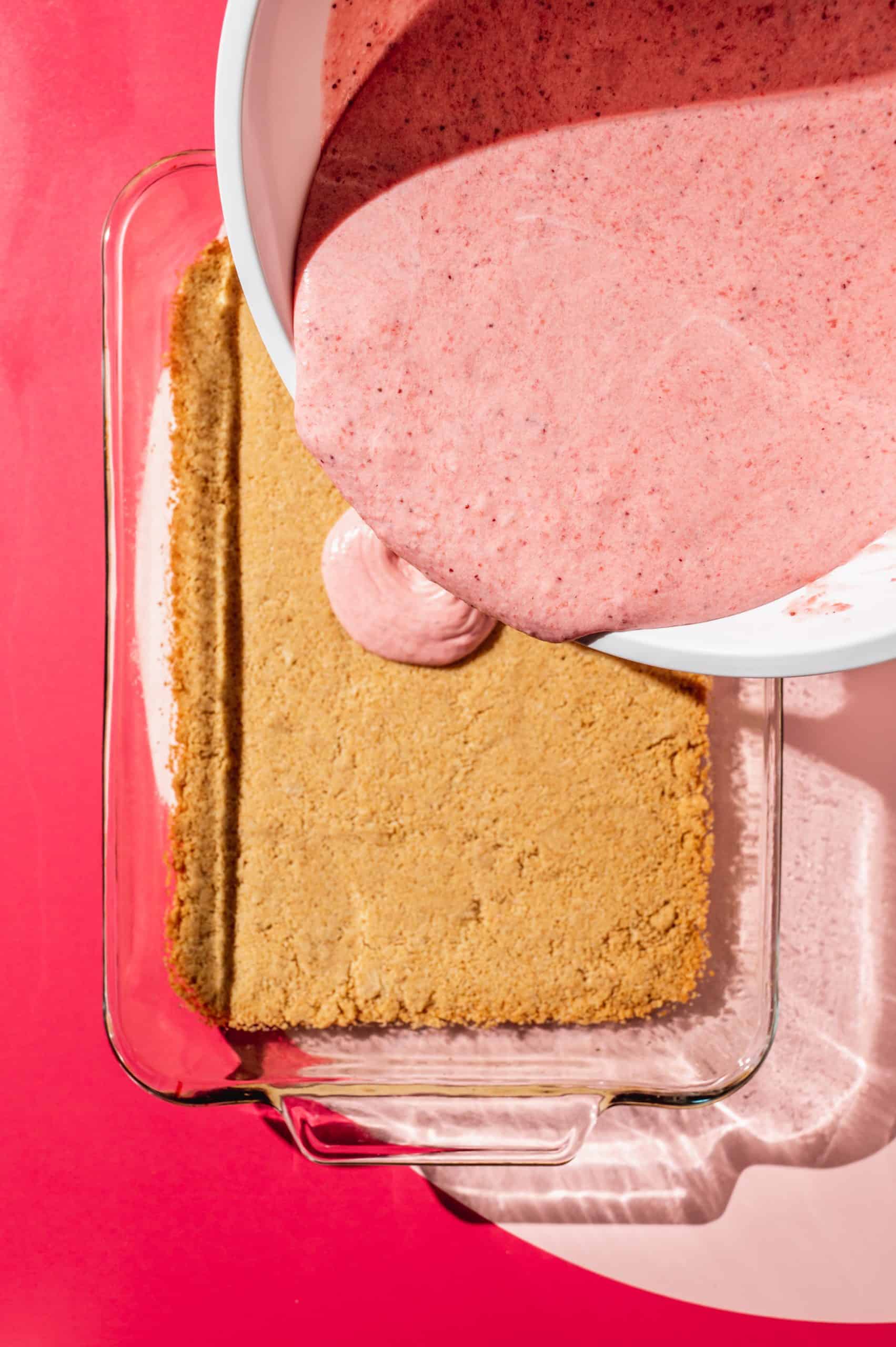 pouring bowl of strawberry mousse filling over the pre-baked graham cracker pie crust