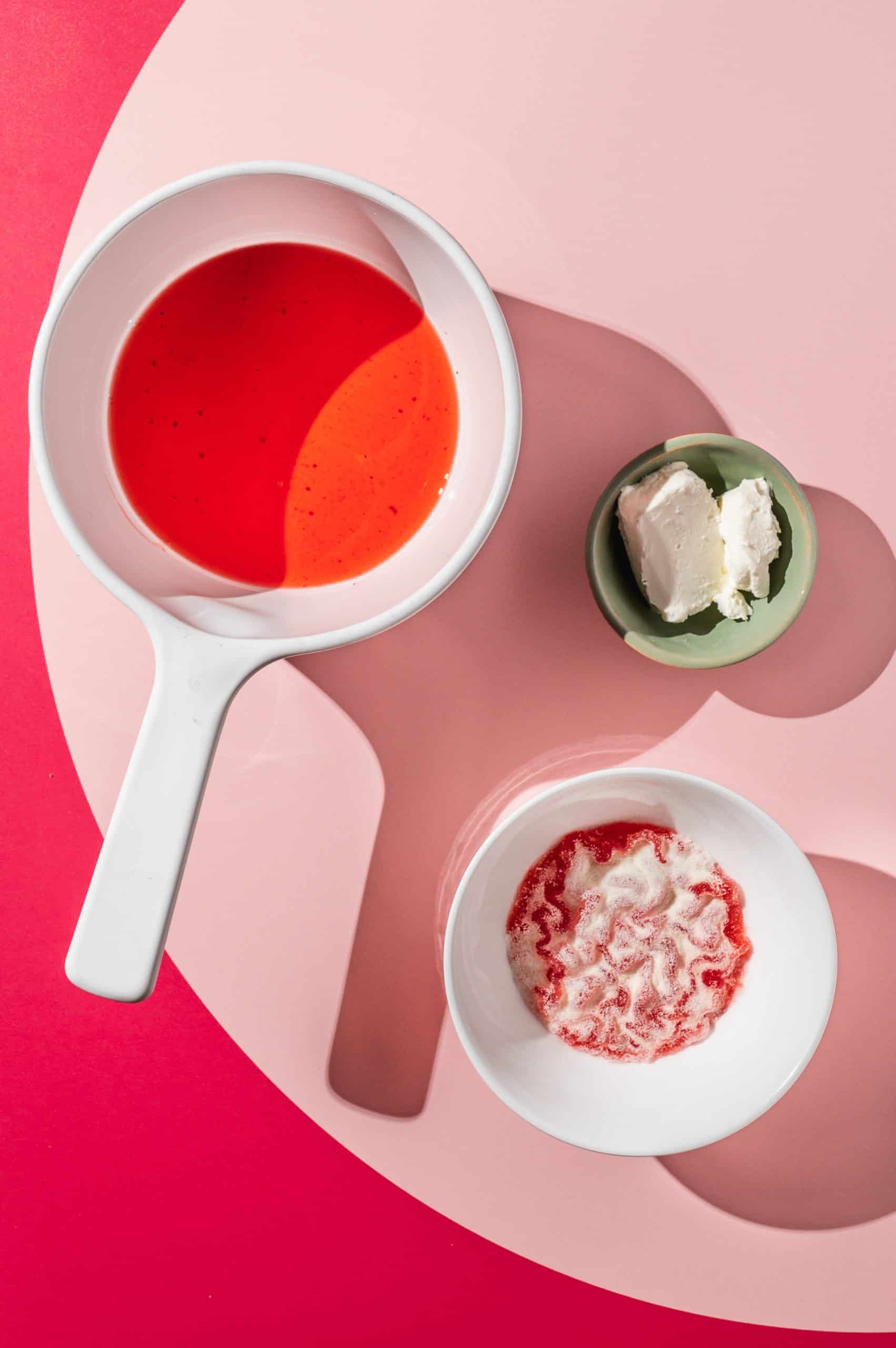 small white pot with strawberry juice next to small bowl of cream cheese and small bowl of bloomed gelatin