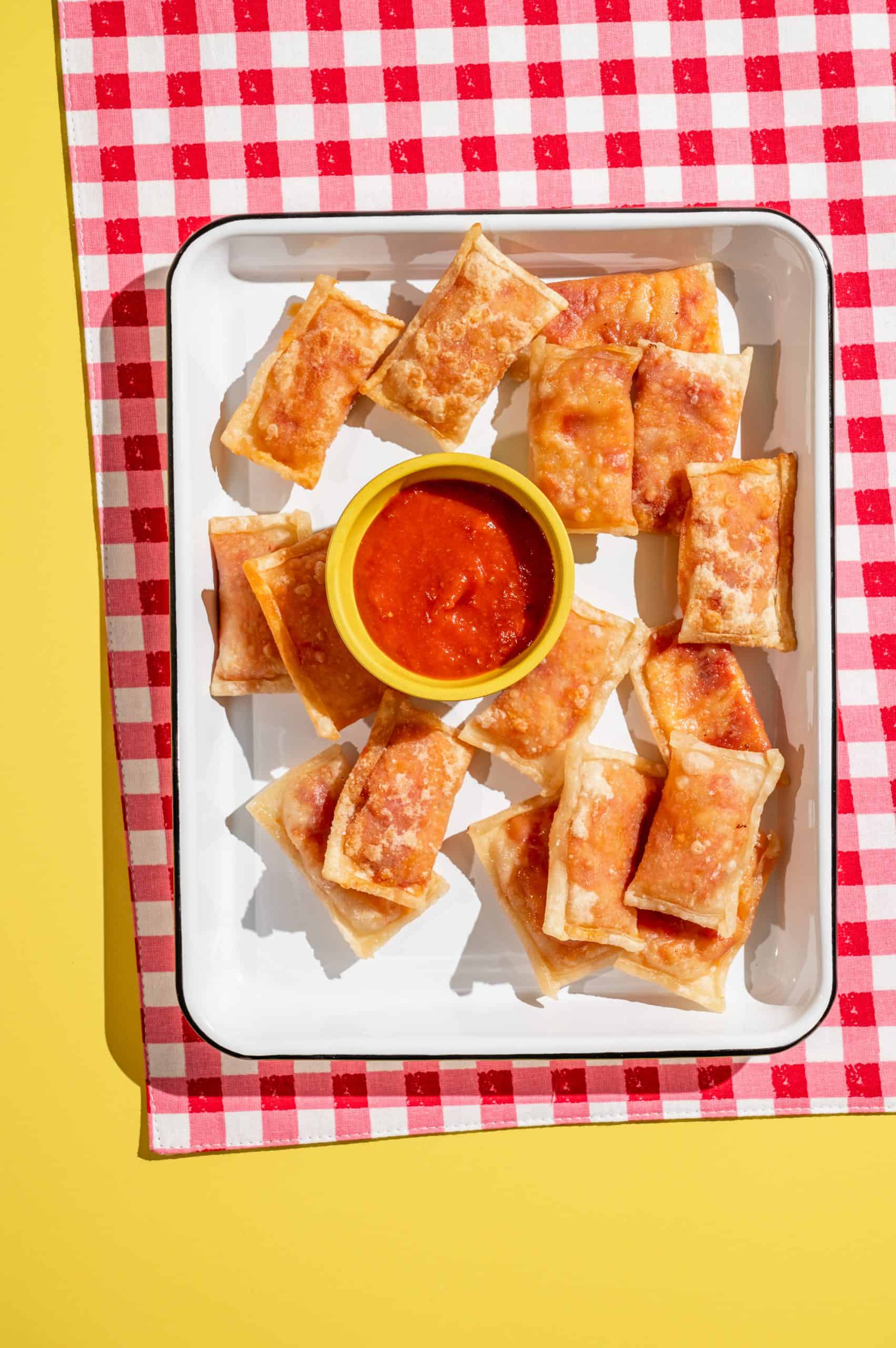 homemade pizza rolls on a white tray with cup of marinara dipping sauce on the side