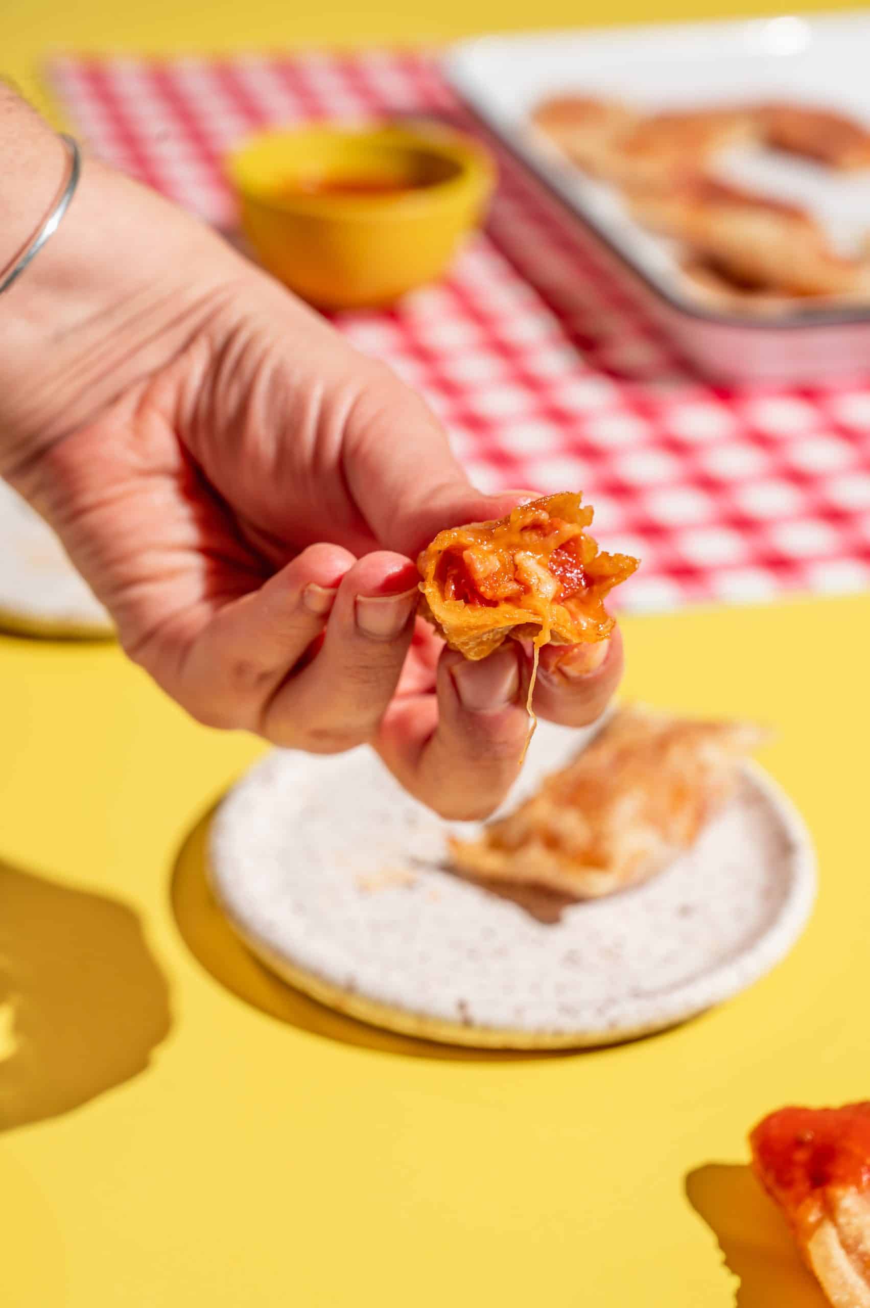 hand holding a homemade pizza roll with a bite taken out, melted cheese filling oozing out