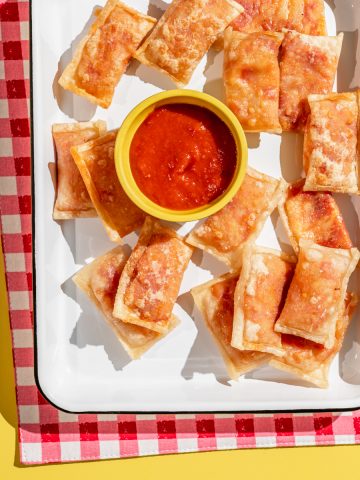 homemade pizza rolls on a white tray with cup of marinara dipping sauce on the side