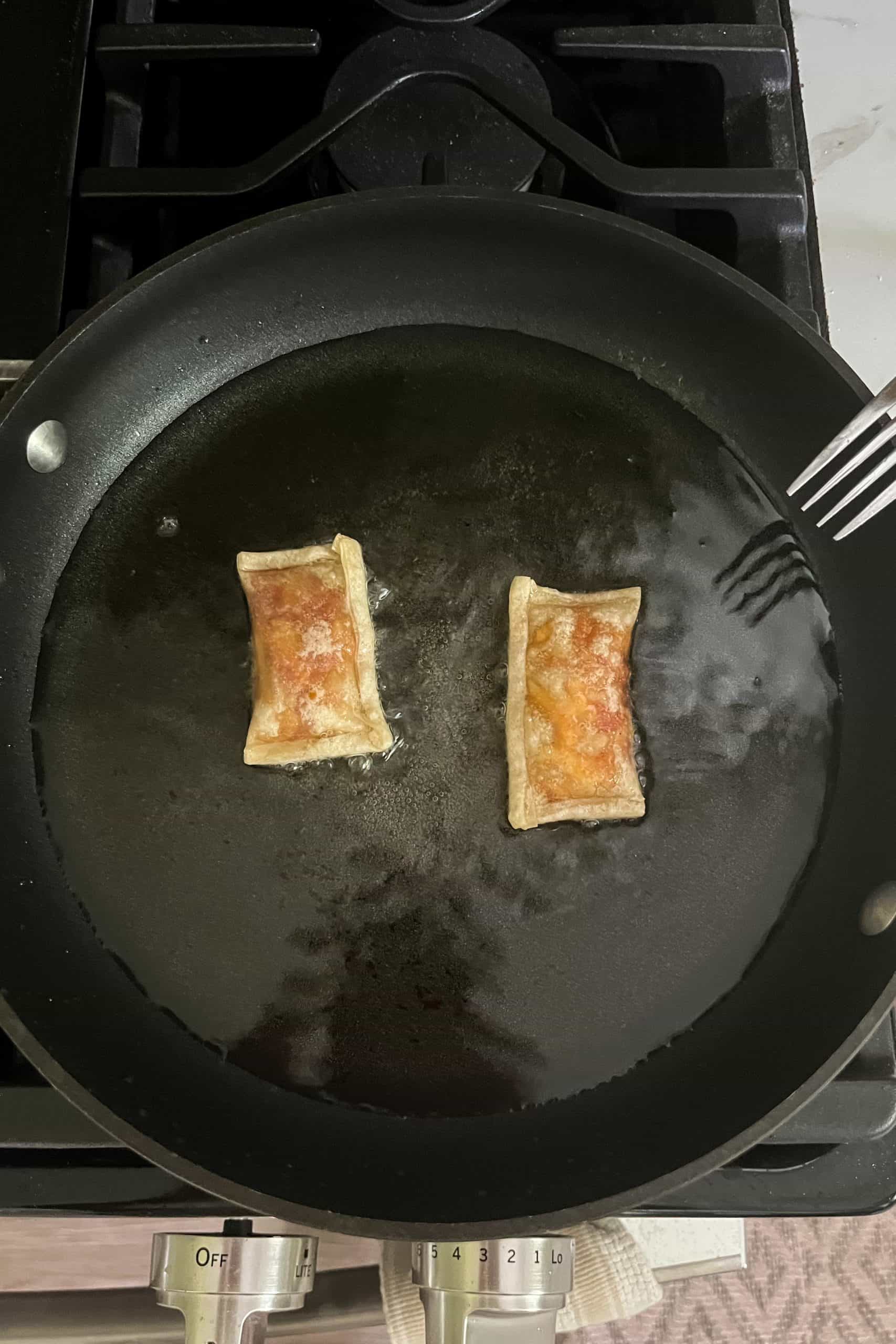 two homemade pizza rolls being fried in a pan with a thin layer of oil