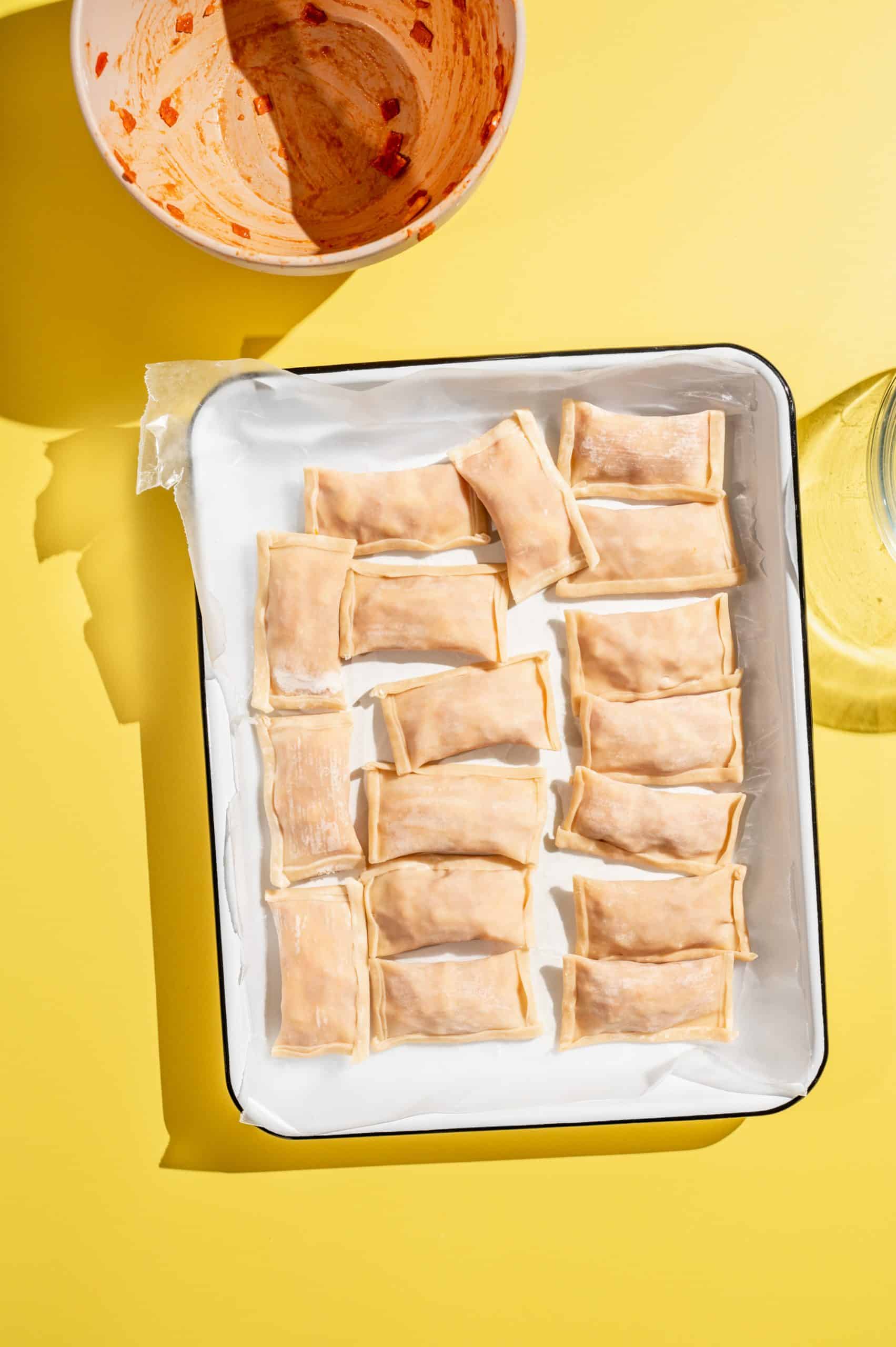 white tray with 17 raw homemade pizza rolls, assembled but not yet fried