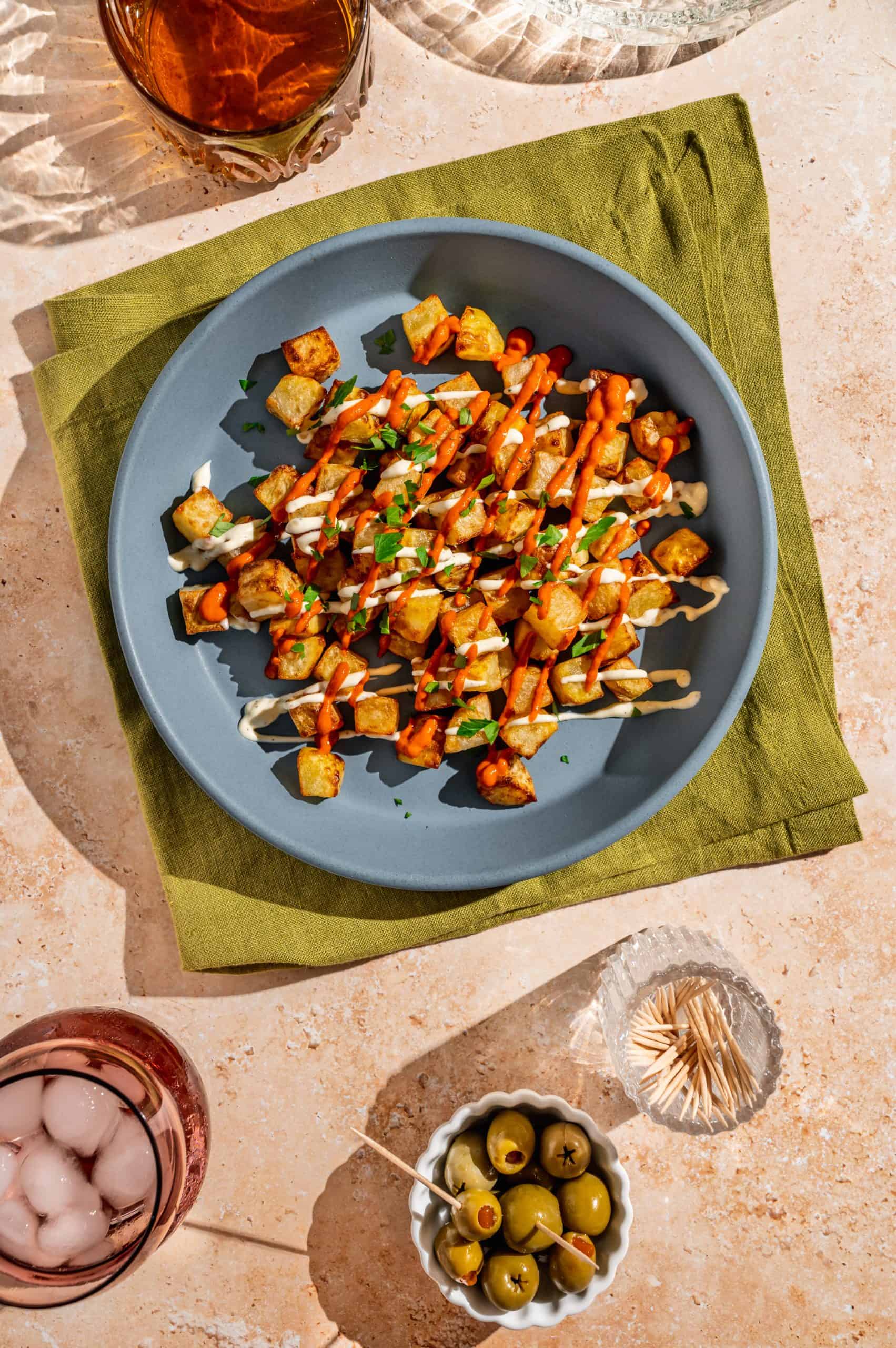 diced potatoes in a shallow dish drizzled with bravas sauce and aioli, garnished with chopped parsley