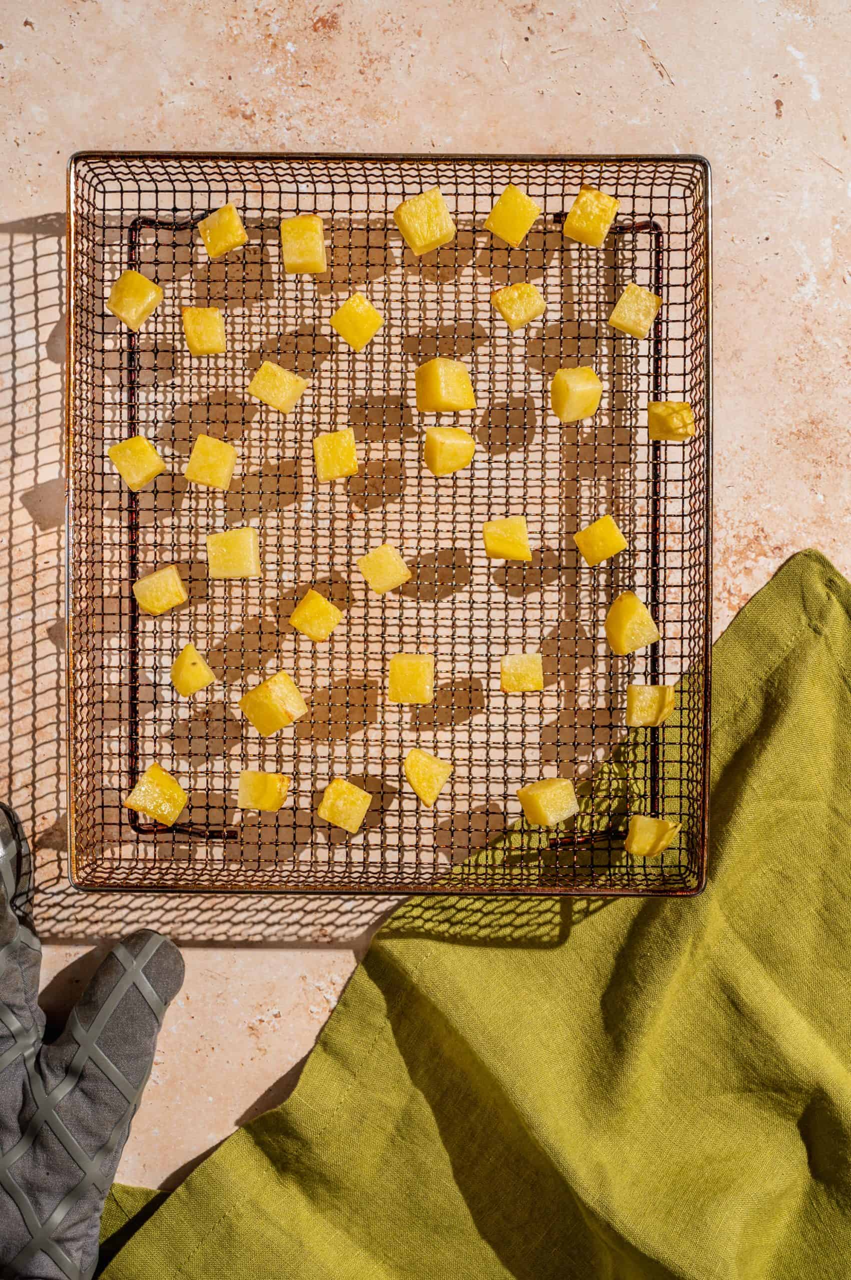 air fryer basket with partially cooked diced potatoes, dried on the surface but no color