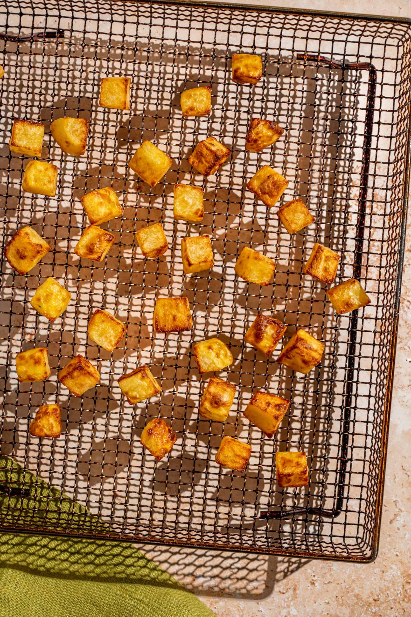 air fryer basket with crispy golden brown diced potatoes evenly spaced out