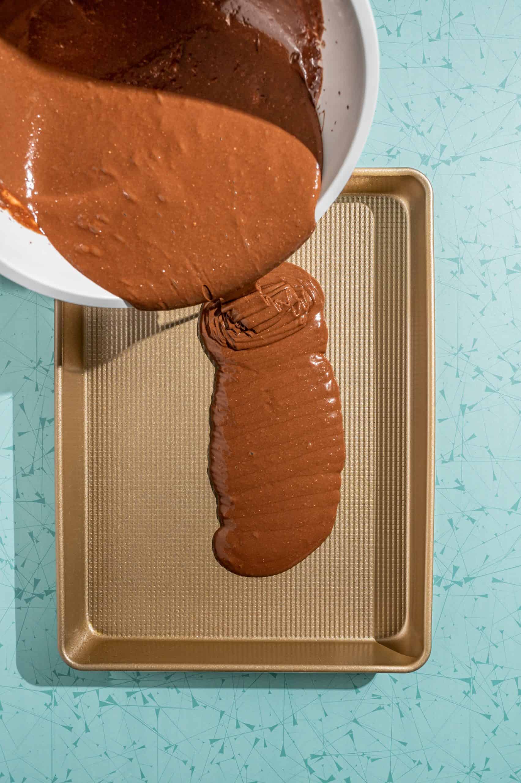 pouring chocolate cake batter into a shallow rectangular baking pan