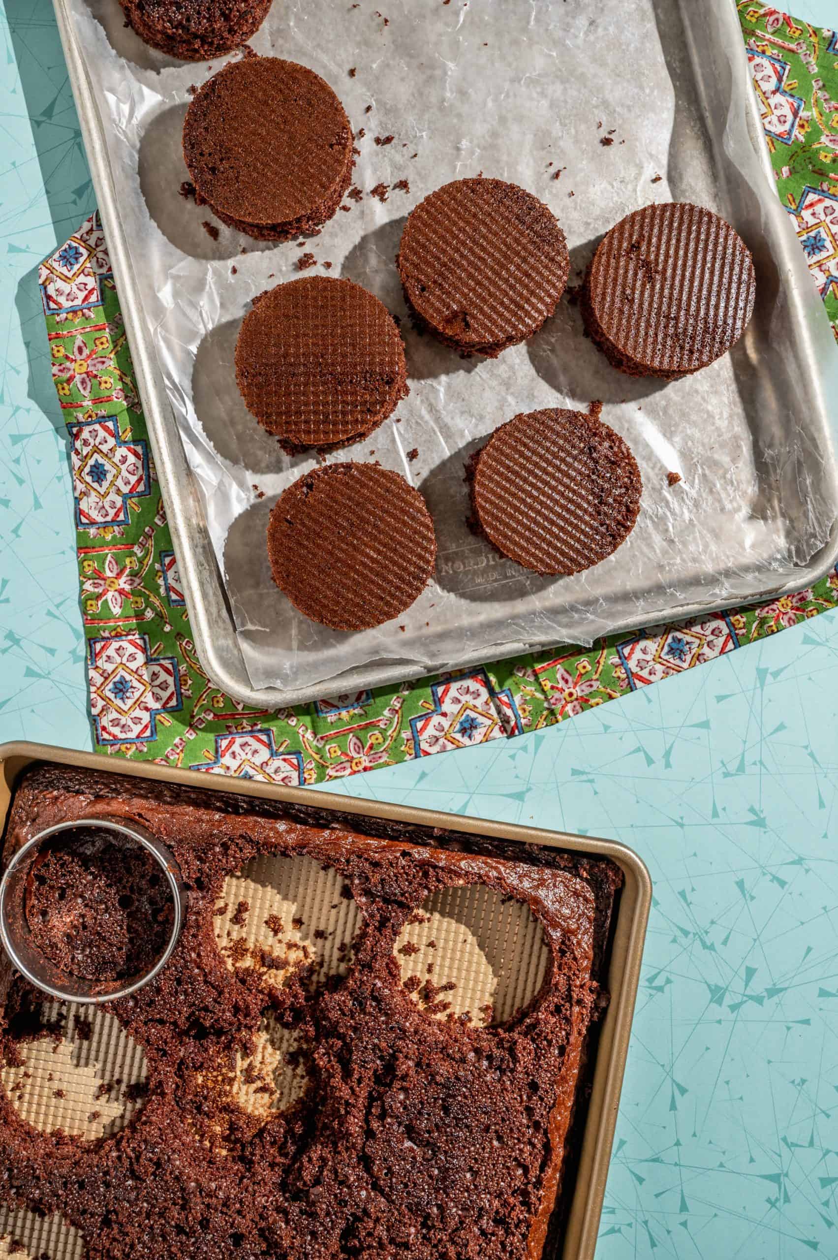 sheet cake with circles cut out of it and a lined baking sheet with mini circular chocolate cakes