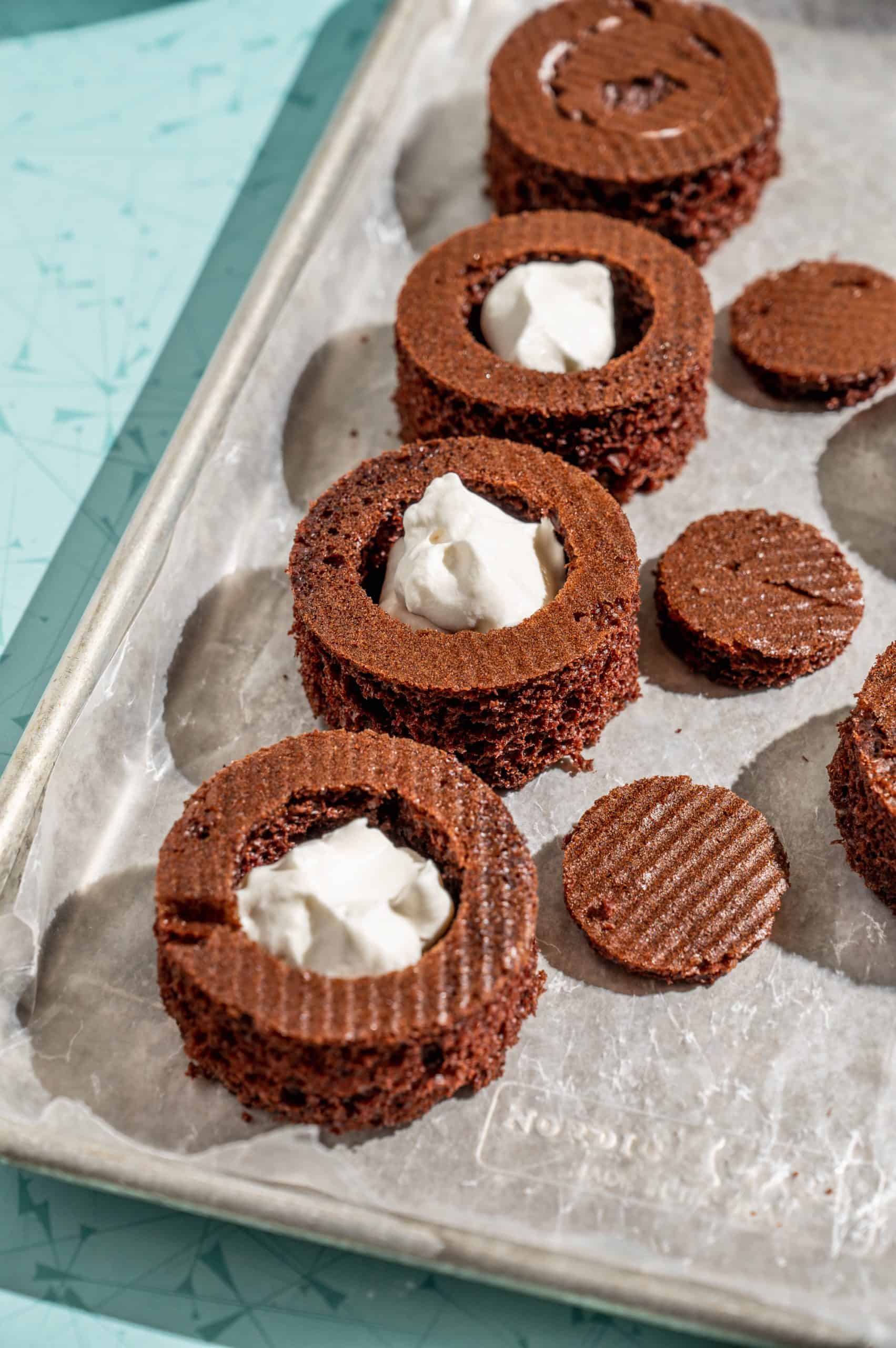 baking sheet with 4 ding dongs filled with whipped cream, one with the top replaced to conceal the cream center