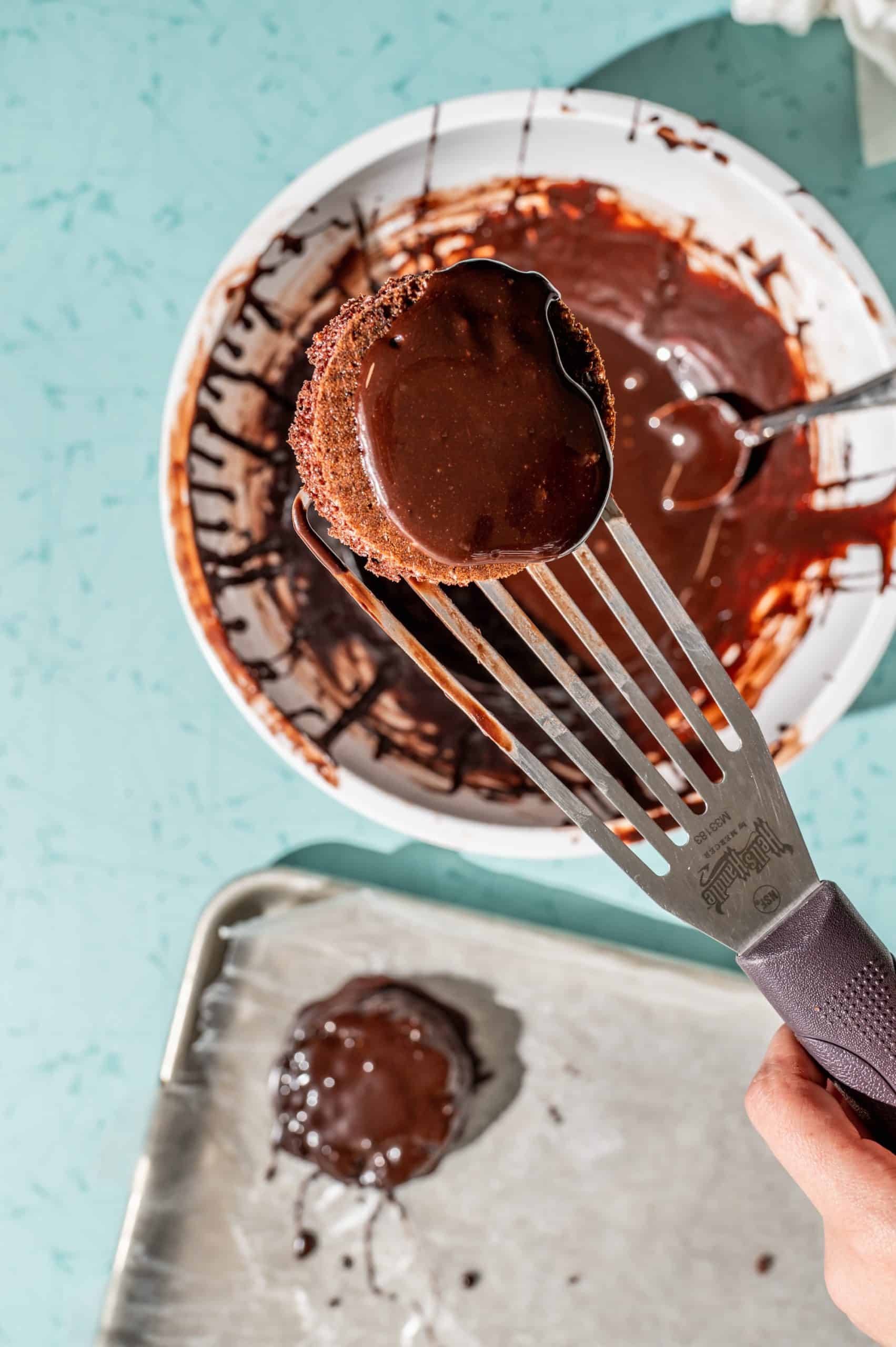 holding a slotted spatula with a ding dong on it above the bowl with chocolate glaze