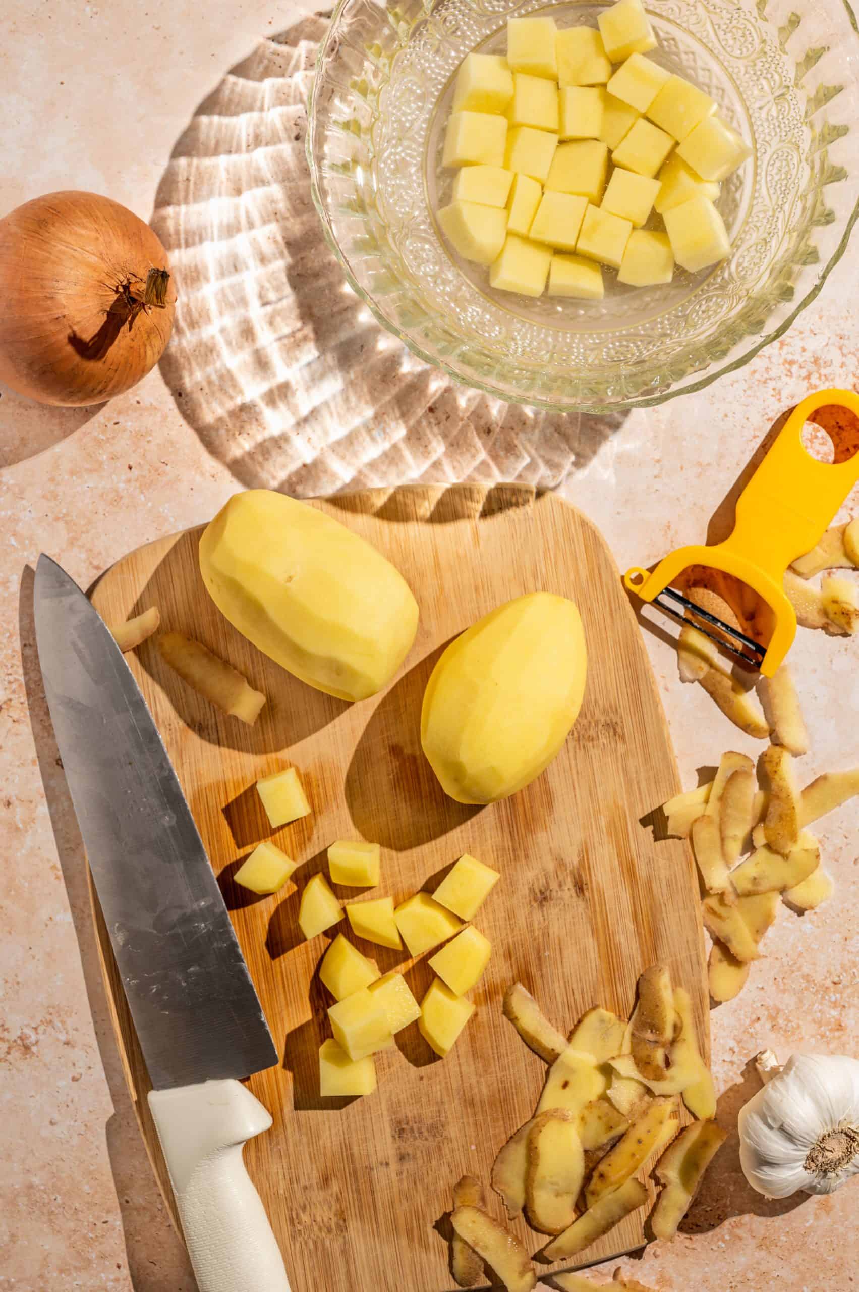 cutting board with 2 whole peeled potatoes and one diced into ¾ inch cubes