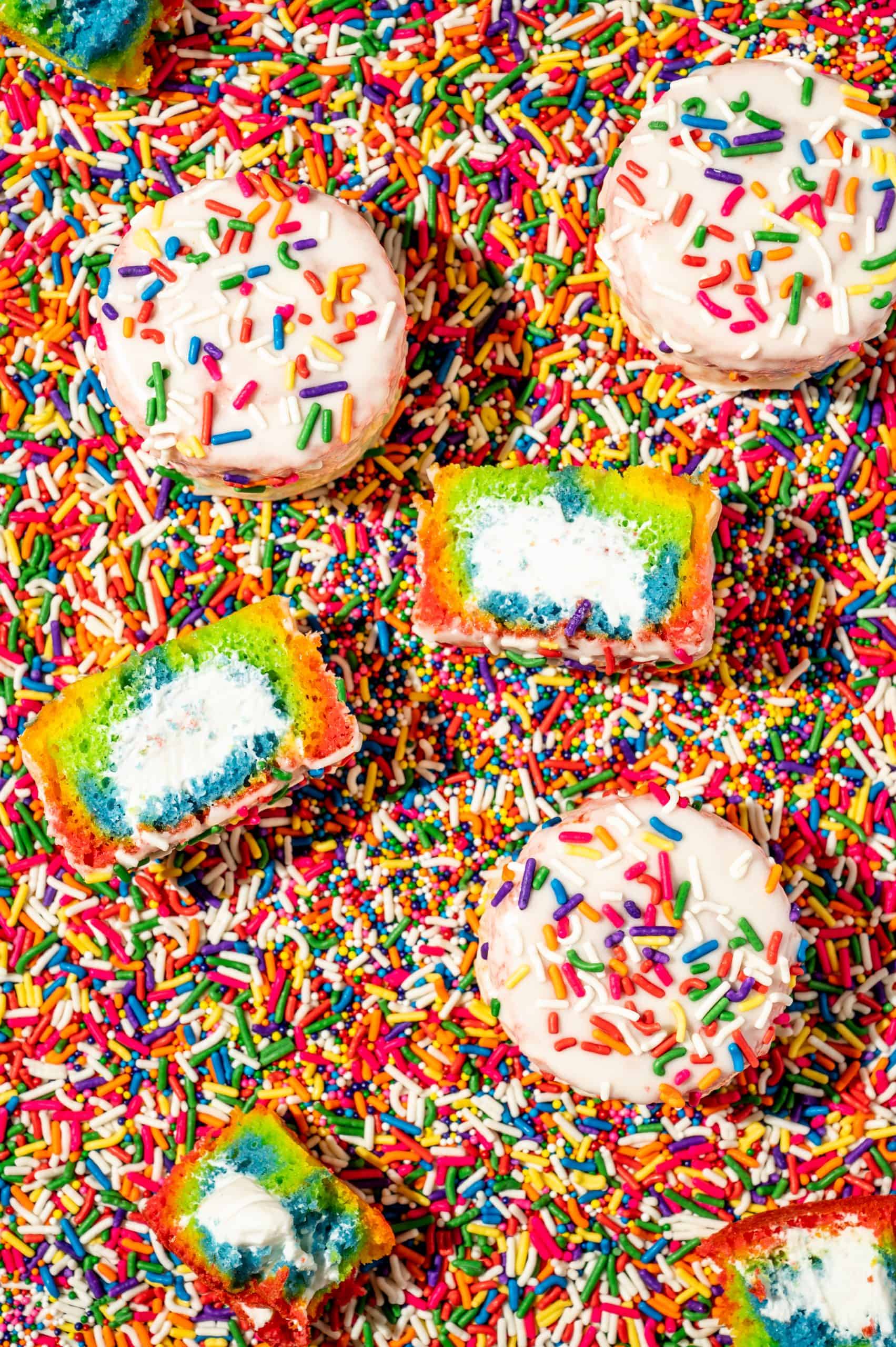 vanilla ding dongs with rainbow sprinkles, 1 cut in half to reveal rainbow cake and creme filling