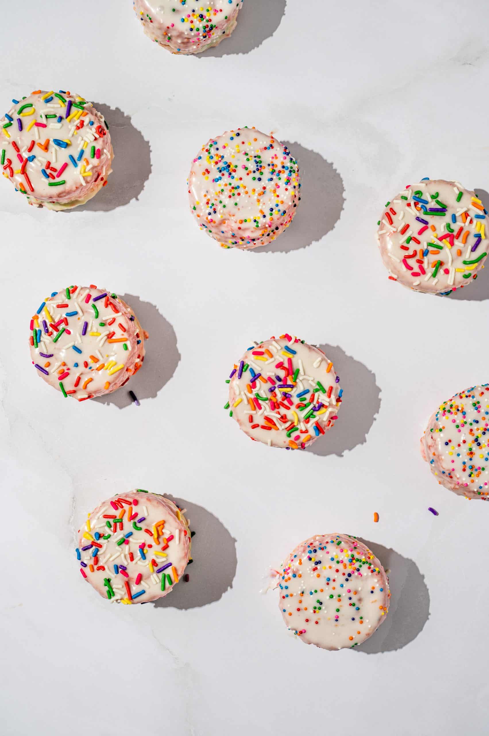 9 vanilla ding dongs with rainbow sprinkles from overhead on a marble surface