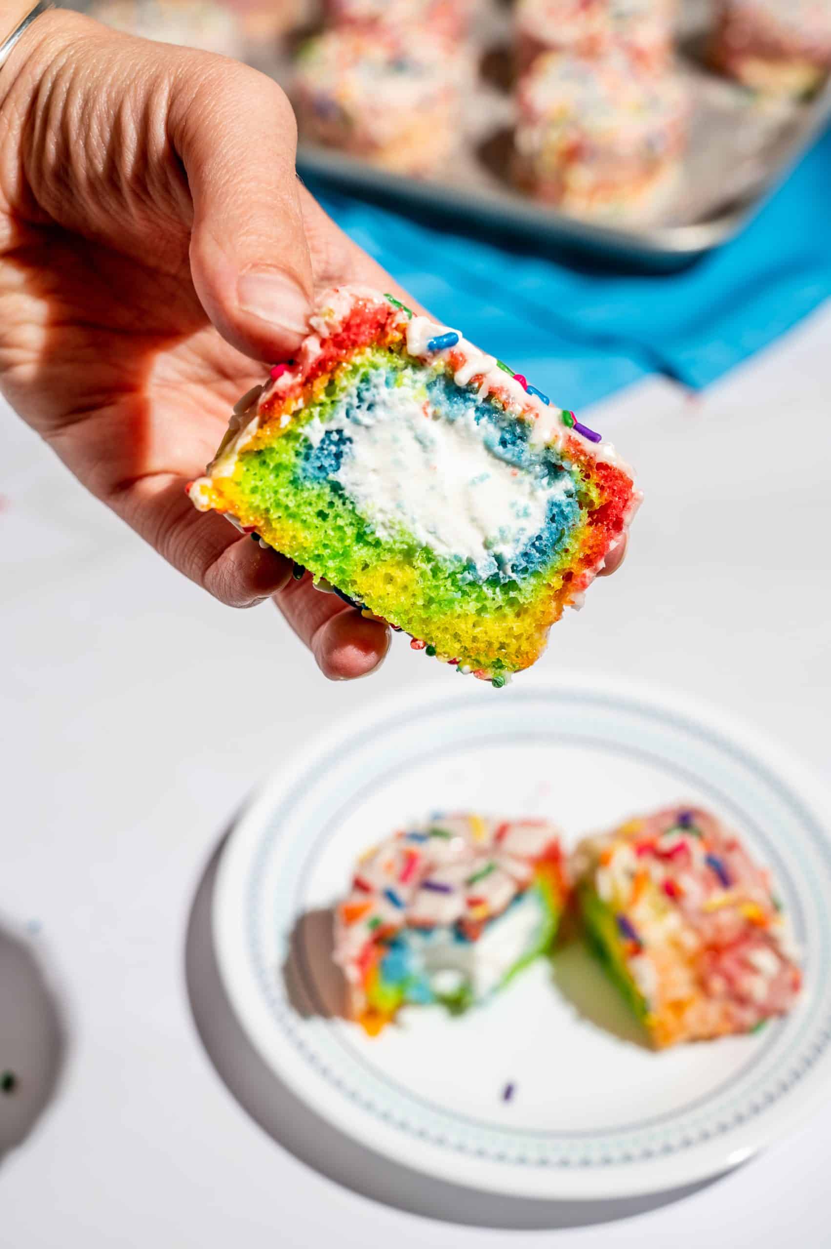 hand holding half of a rainbow vanilla ding dong to show the whipped cream filling inside