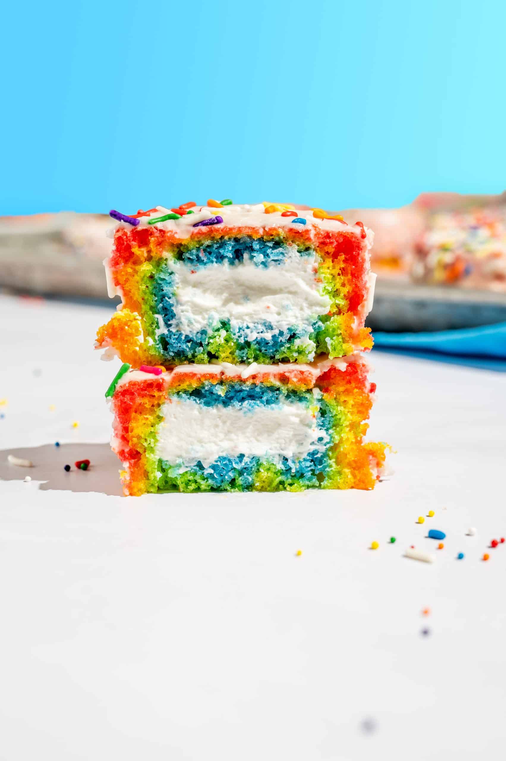 straight on view of a rainbow vanilla ding dong sliced in half and stacked to reveal rainbow cake and whipped cream filling