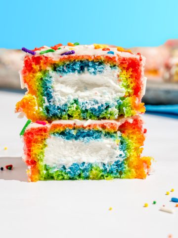 straight on view of a rainbow vanilla ding dong sliced in half and stacked to reveal rainbow cake and whipped cream filling