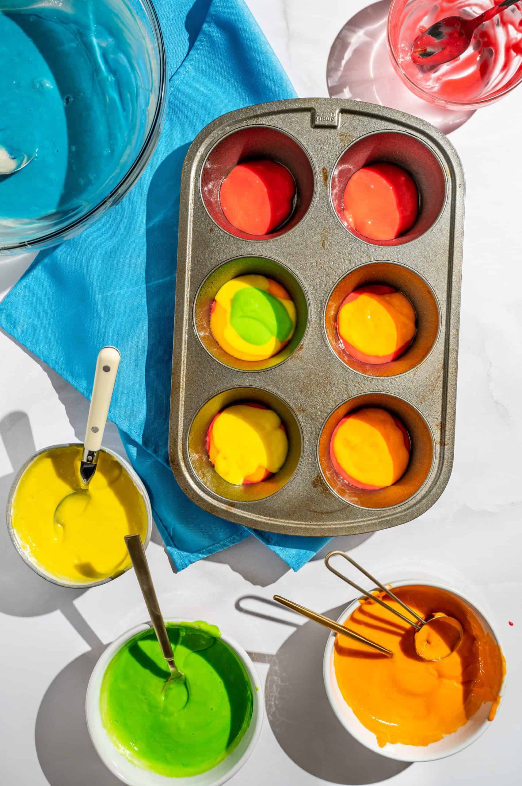 jumbo muffin tin filled with layers of different colors of dyed vanilla cake batter to create a rainbow design